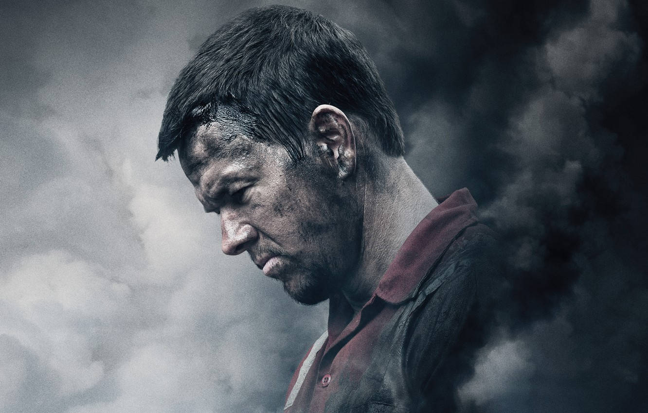 Mark Wahlberg 桌布 壁紙 — 一個骯髒的男人穿著紅色有領襯衫，在陰雲密佈的背景中，凝視著旋轉的黑煙。