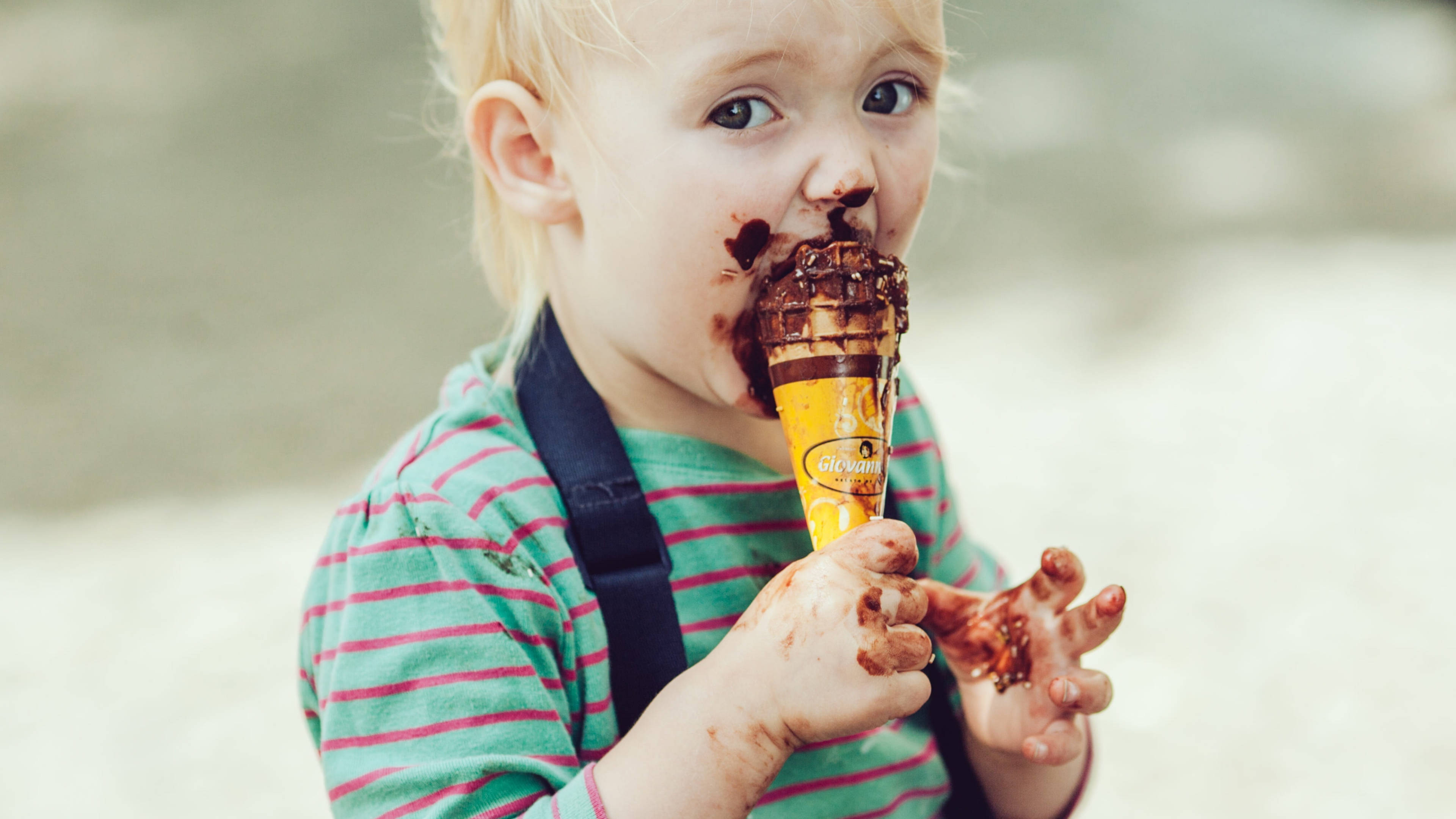 Chocolate Day 桌布 壁紙 — 一個髒兮兮的幼兒，臉上和手上沾滿巧克力，開心地吃著巧克力冰淇淋甜筒。