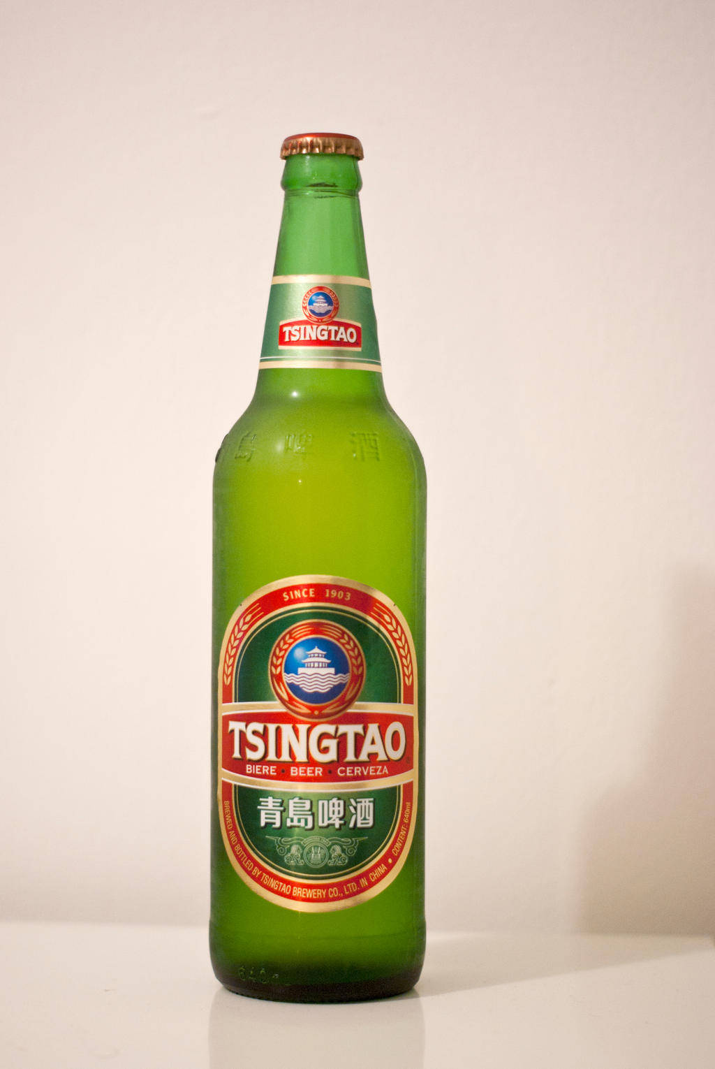 booze 桌布 壁紙 — 一個高大的綠色青島啤酒瓶在柔和的燈光下直立於純白色背景前。