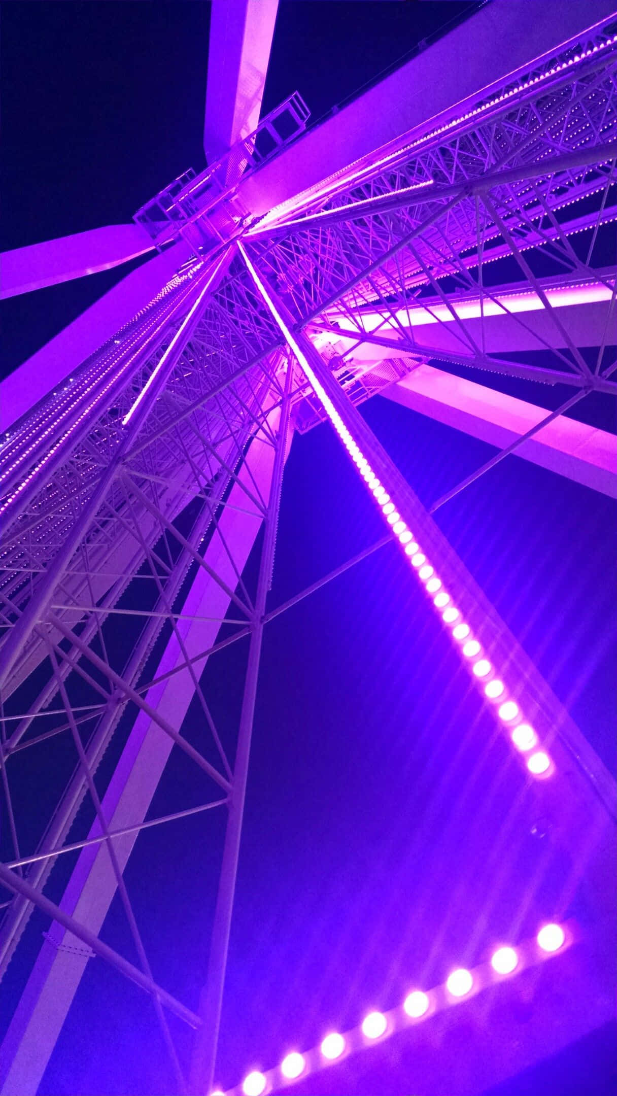 lights 桌布 壁紙 — 一個高聳的摩天輪在低角度拍攝下，以鮮豔的紫色燈光在漆黑的夜空中閃耀。