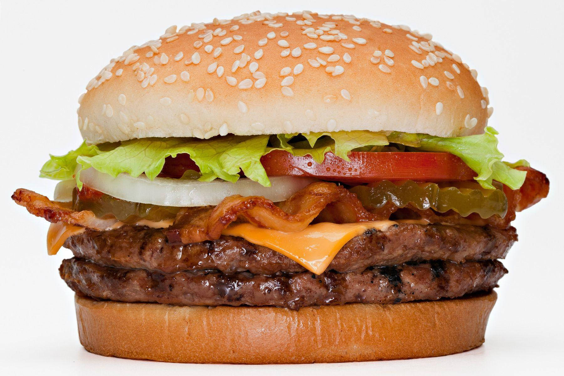 Burger King 桌布 壁紙 — 一個高聳的雙層漢堡，配以芝麻麵包、融化起司、培根、番茄、生菜和洋蔥，在純白背景上高高疊起。