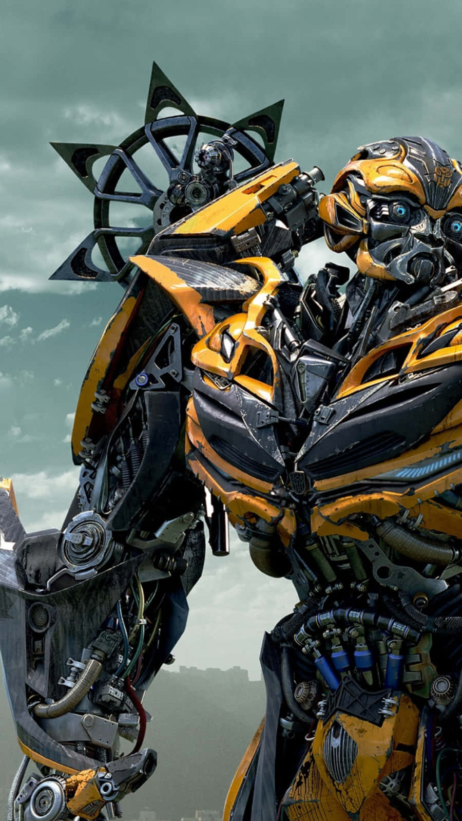 Bumblebee 桌布 壁紙 — 一個高聳的黃黑機器人，帶有複雜的機械細節，矗立在多雲的天空下。