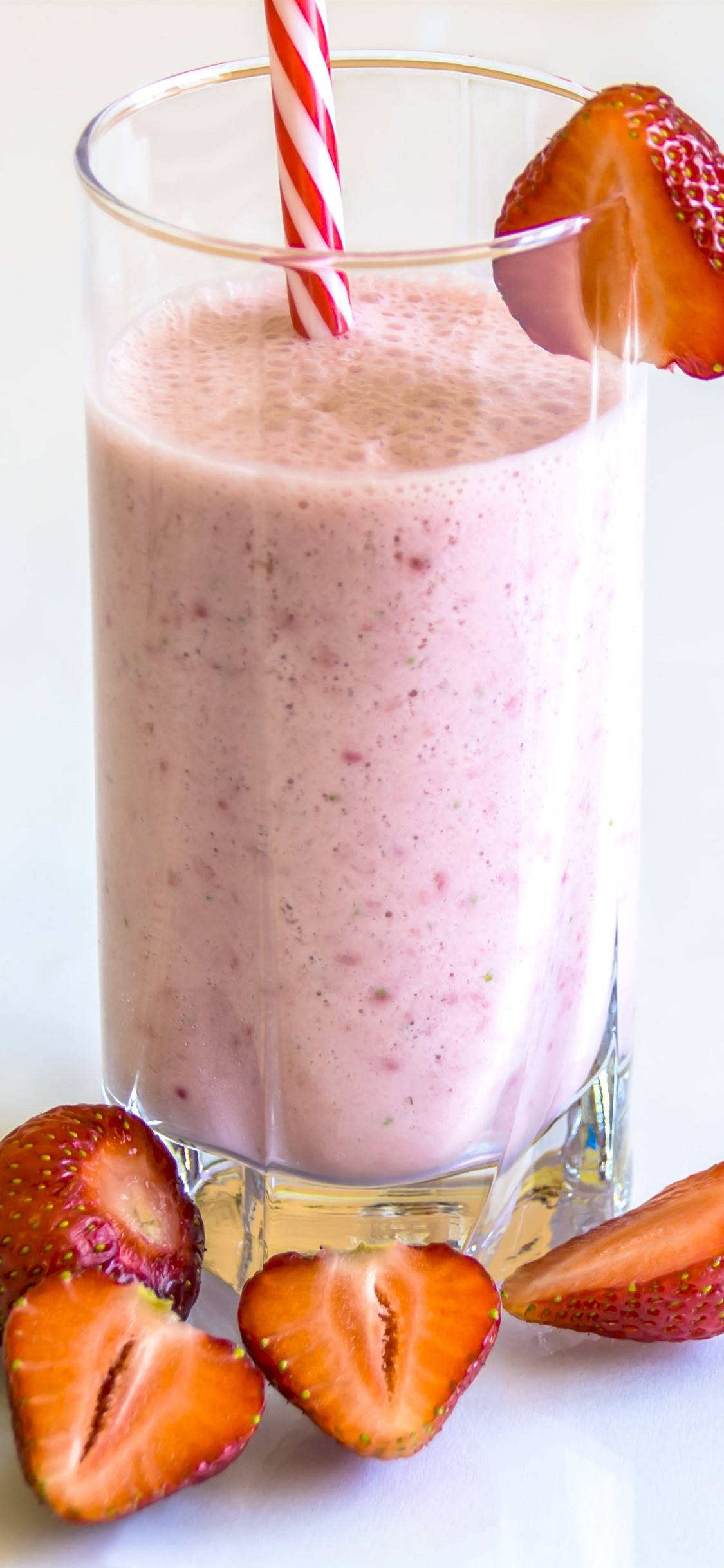 Smoothie 桌布 壁紙 — 一個高身玻璃杯裝滿粉紅色草莓奶昔，上面插著紅白條紋吸管，並以新鮮切片草莓裝飾。