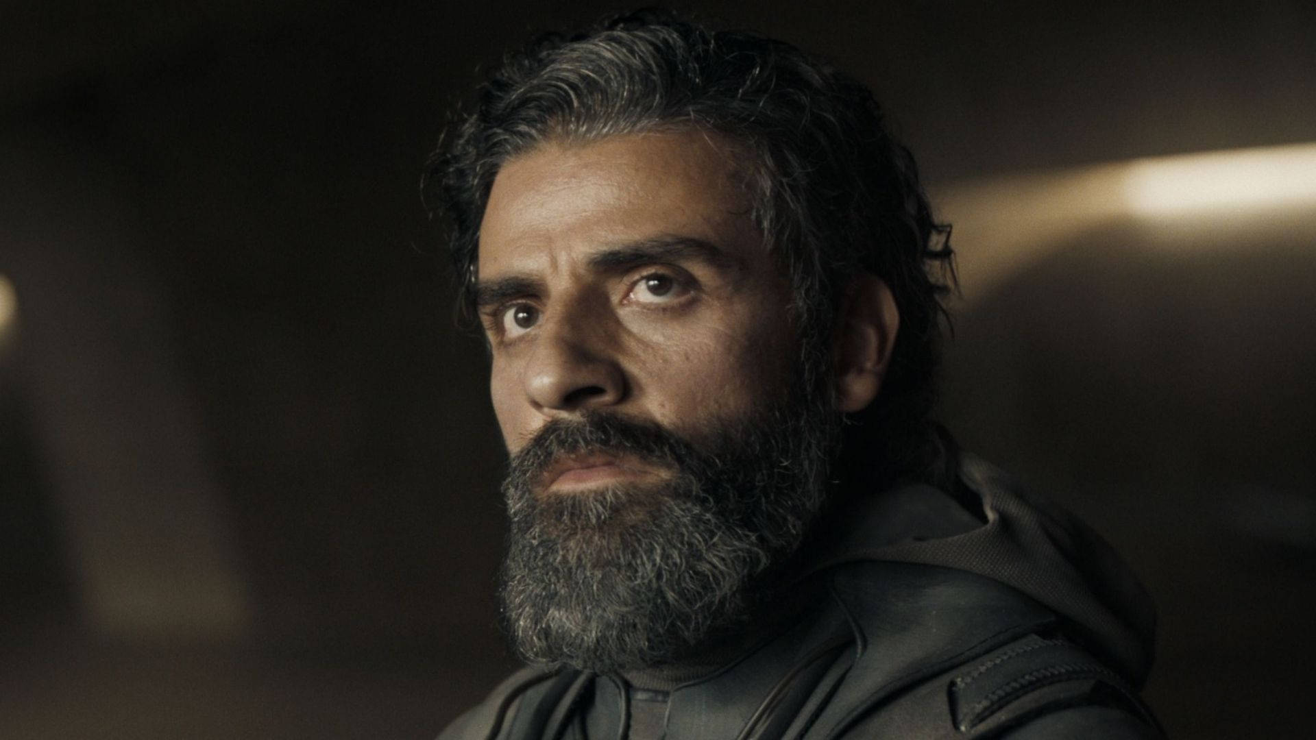oscar 桌布 壁紙 — 一個鬍子花白、眼神銳利的男人，在昏暗且充滿氛圍的室內直視前方。