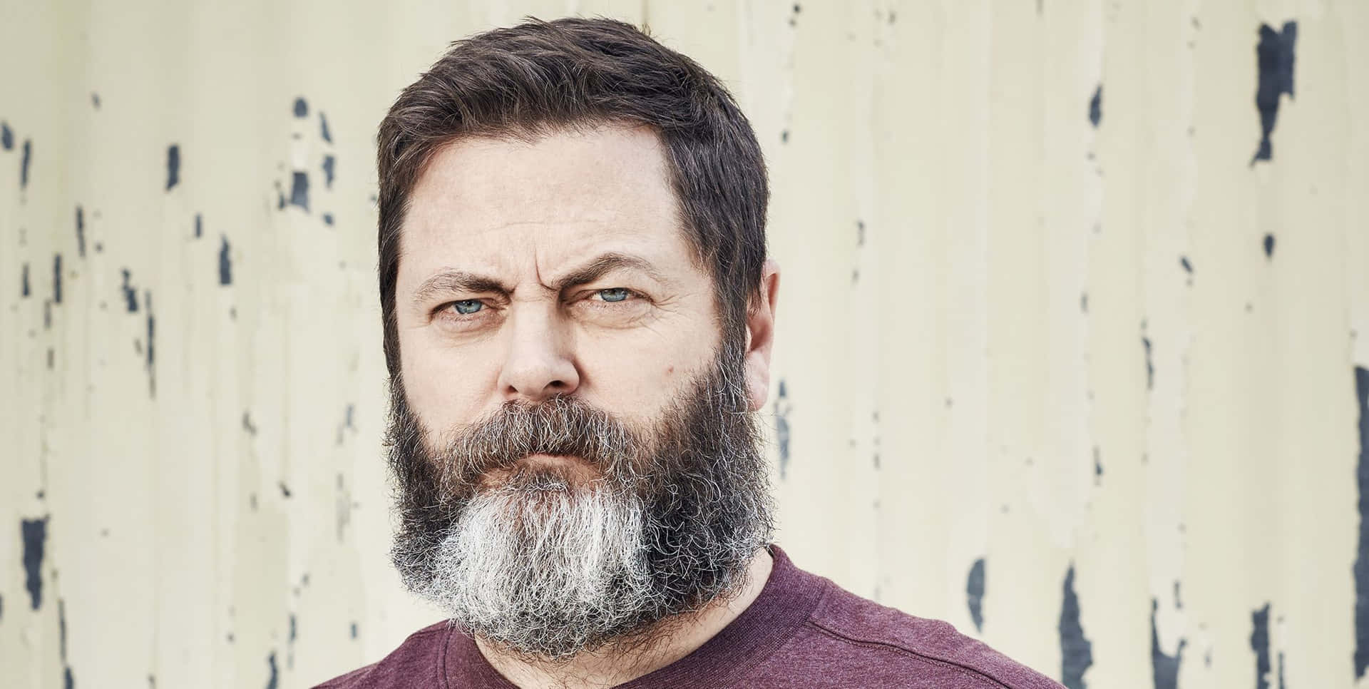 nick offerman 桌布 壁紙 — 一個鬍子花白、眼神銳利的男人，在風化剝落的牆壁前直視鏡頭。