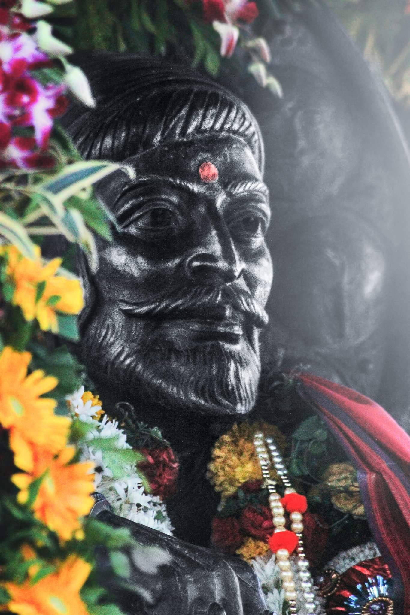 Indian 桌布 壁紙 — 一個鬍鬚男人的深色石像特寫，裝飾著鮮豔的花環和紅色珠子。