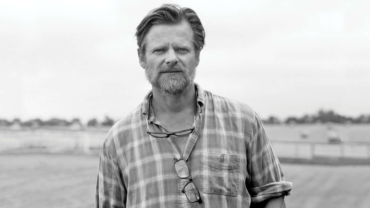 Steve Zahn 桌布 壁紙 — 一個鬍鬚男人穿著格子襯衫，眼鏡掛在脖子上，站在戶外的黑白肖像。