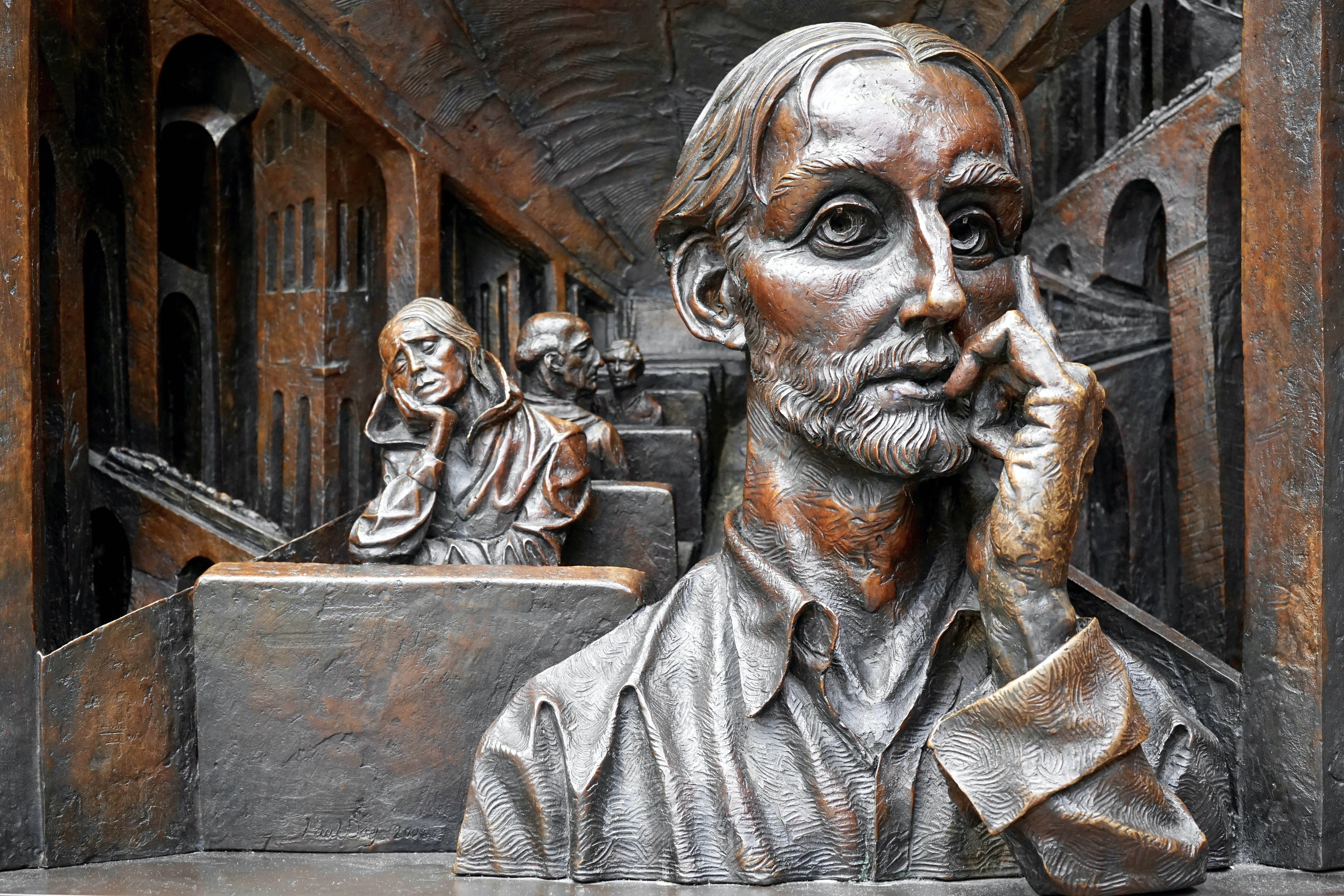 Sculpture 桌布 壁紙 — 一個鬍鬚男子的銅像，呈現沉思姿態，周圍有其他人物和詳細的建築場景。