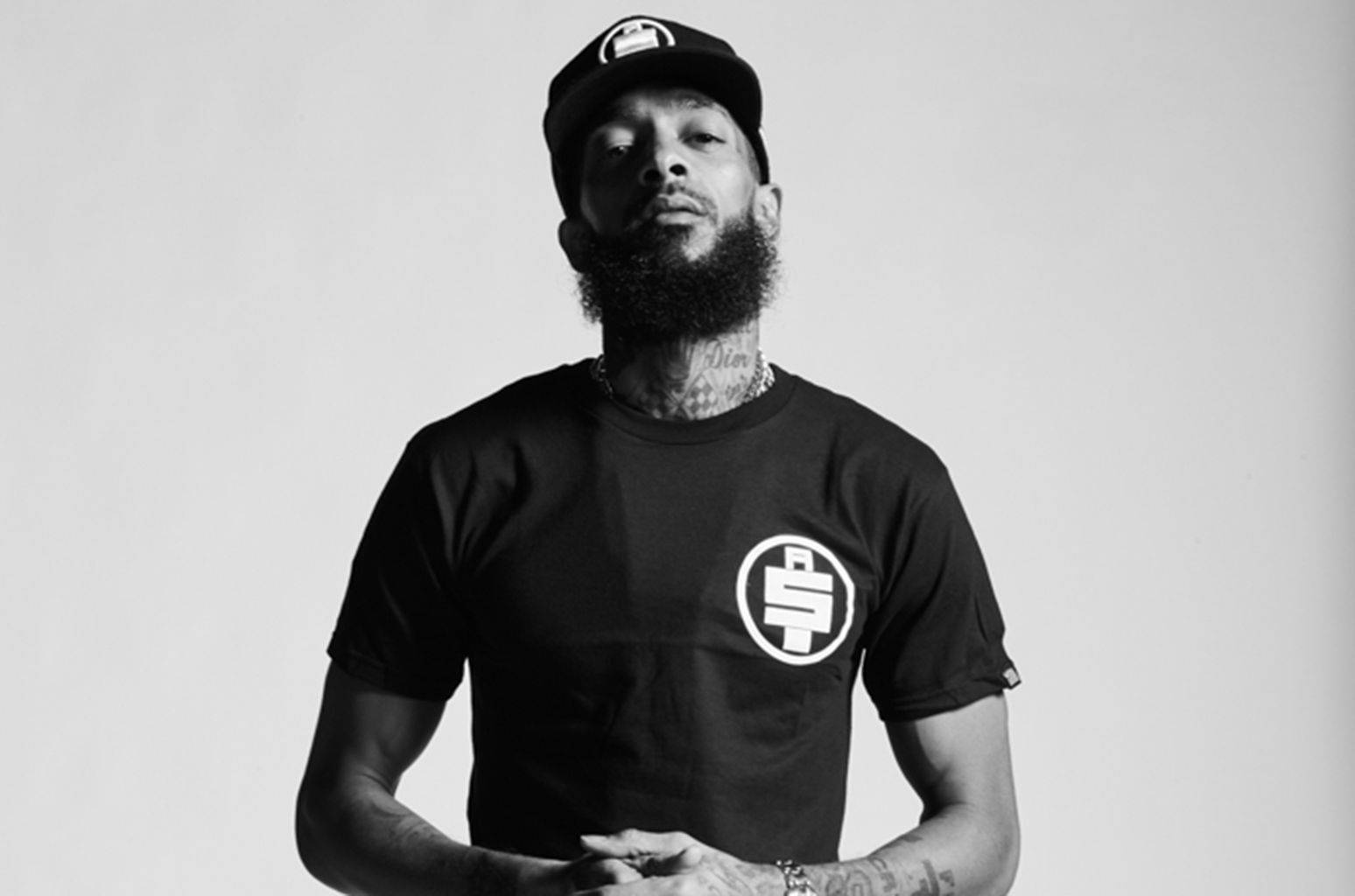 Nipsey Hussle 桌布 壁紙 — 一個鬍鬚男戴帽穿T恤的黑白肖像，頸部和手臂上有刺青。