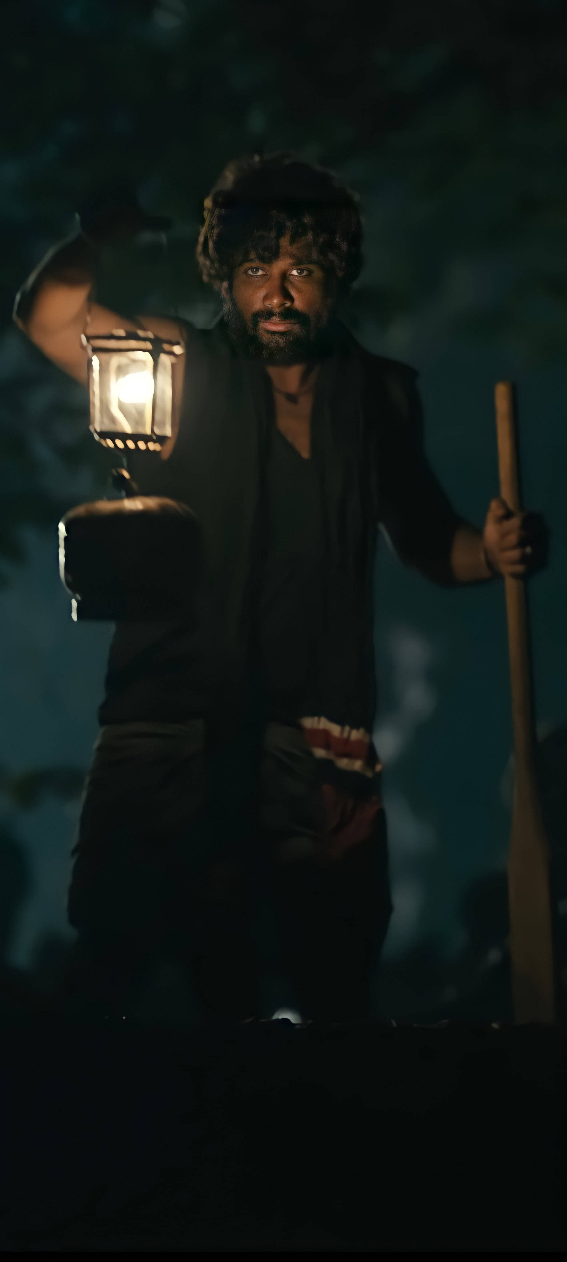 阿盧·阿瓊 桌布 壁紙 — 一個鬍鬚男穿著深色衣服，在陰暗的夜間森林背景下，手持發光燈籠和手杖。