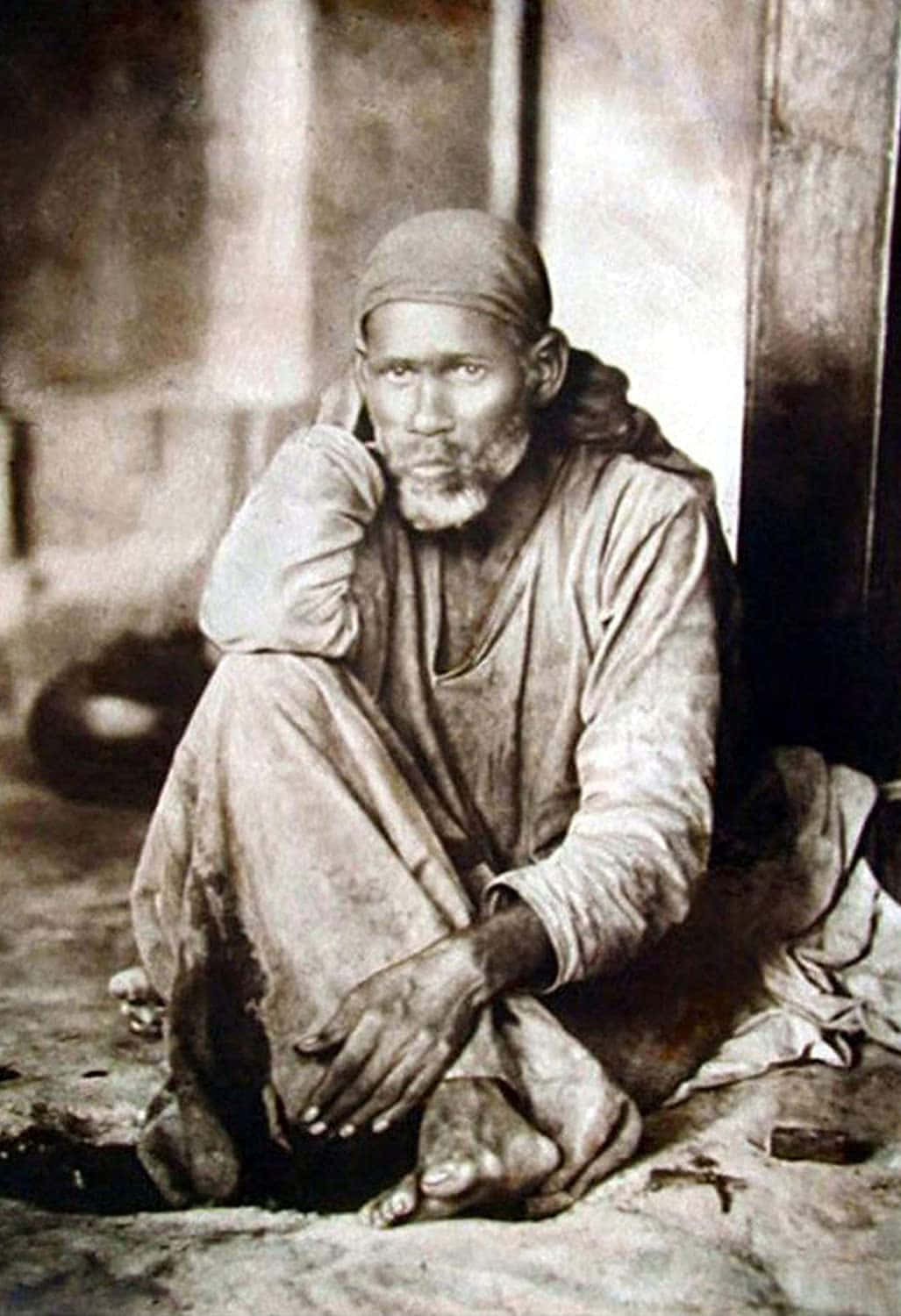 Indian 桌布 壁紙 — 一個鬍鬚蓬鬆的滄桑男人赤腳坐在木牆旁，照片呈復古棕褐色調。