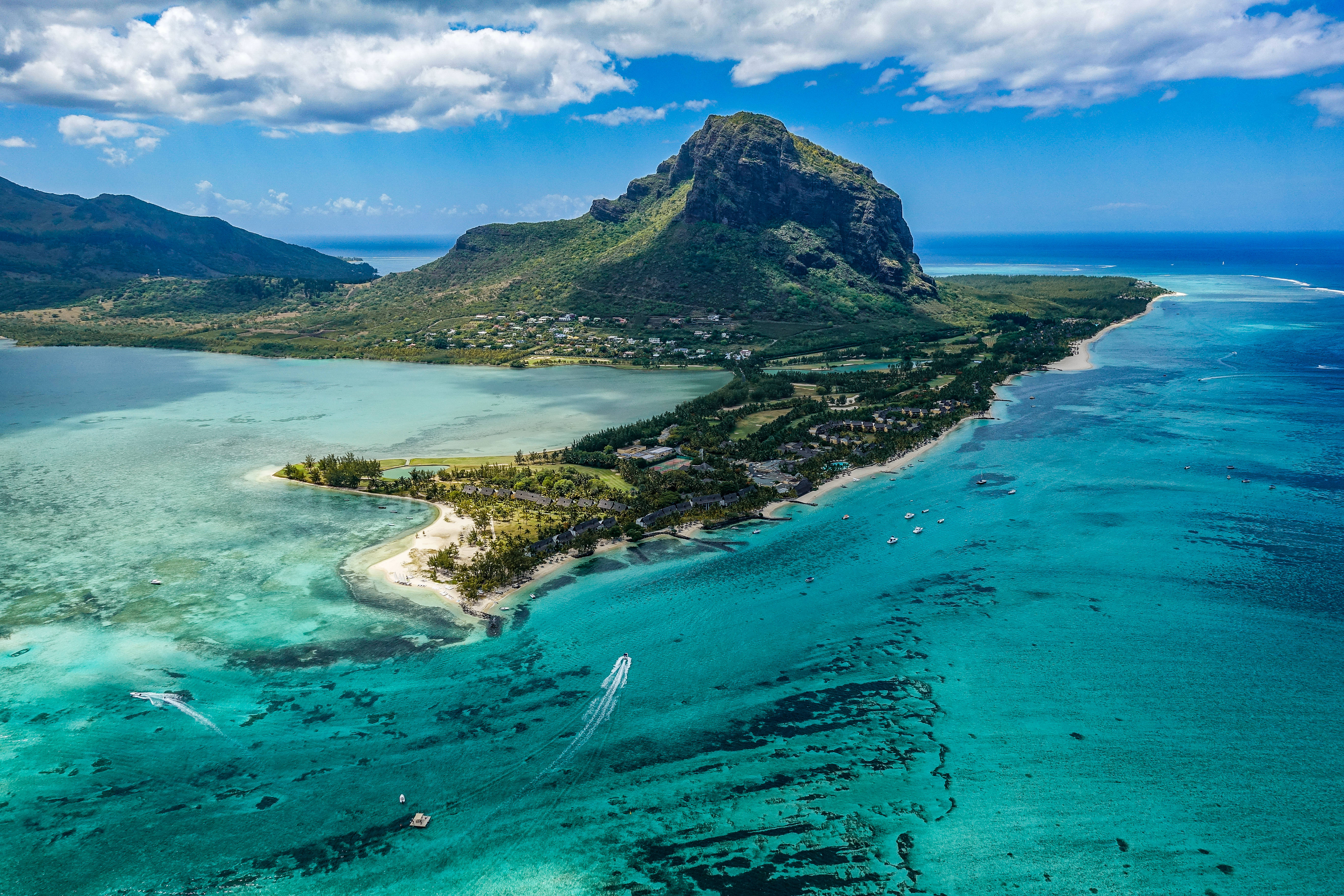 Mauritius 桌布 壁紙 — 一個鬱鬱蔥蔥的熱帶島嶼的鳥瞰圖，一座高聳的綠色山脈從點綴著船隻的碧綠海水中升起。