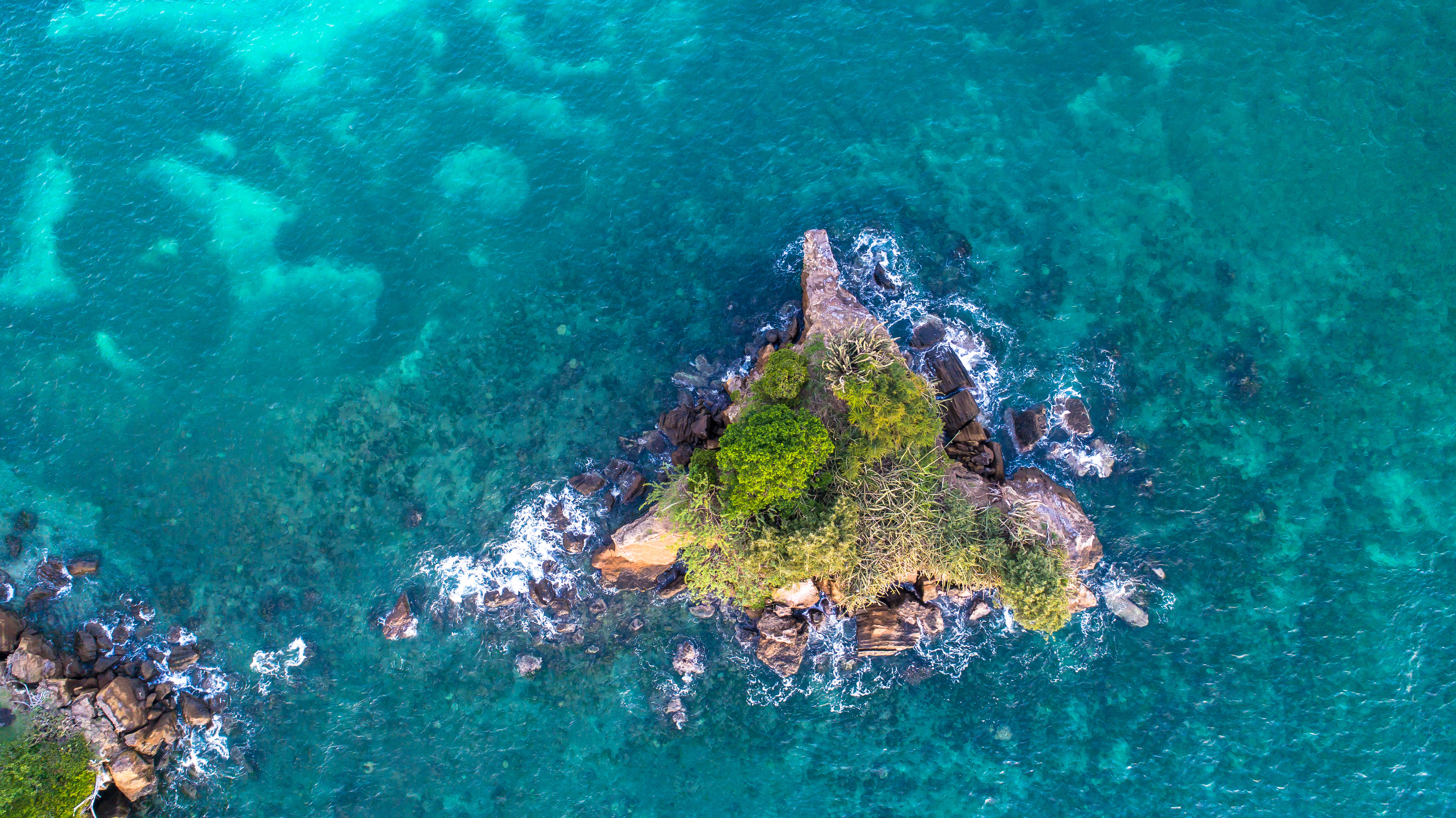 Grenada 桌布 壁紙 — 一個鬱鬱蔥蔥的綠色岩石小島的鳥瞰圖，被充滿活力的藍綠色海水包圍，白色泡沫海浪拍打著海岸。