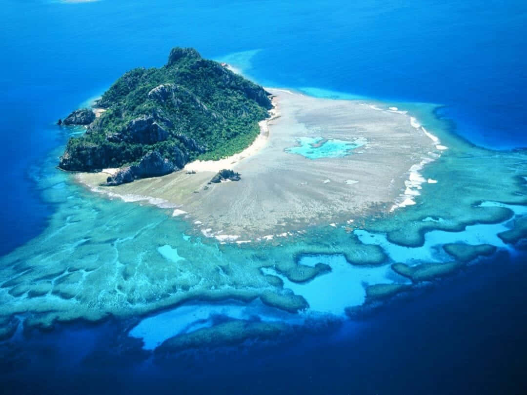 島嶼 桌布 壁紙 — 一個鬱鬱蔥蔥的綠色島嶼的鳥瞰圖，周圍環繞著充滿活力的綠松石珊瑚礁和深藍色的海水。