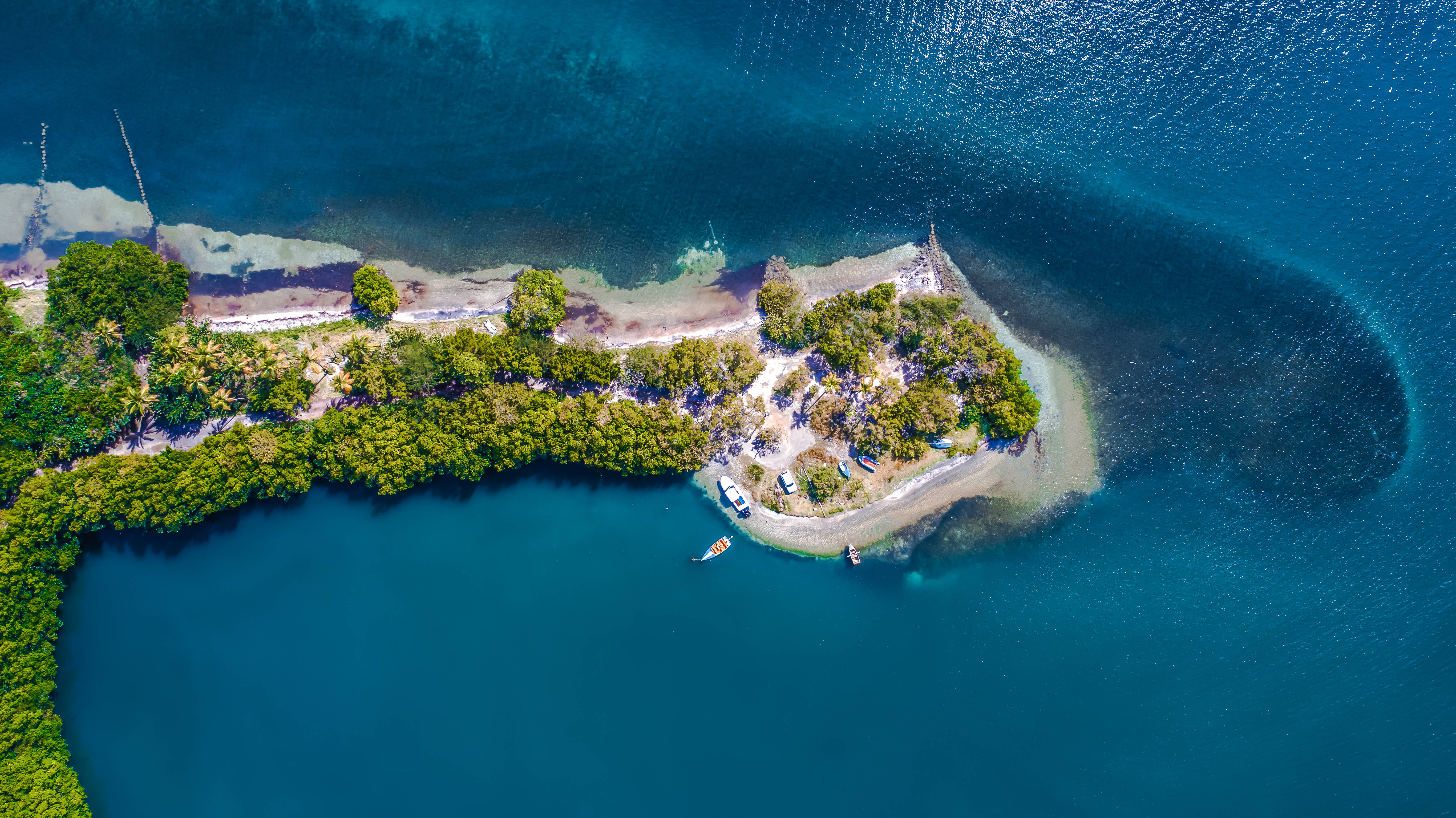Grenada 桌布 壁紙 — 一個鬱鬱蔥蔥的綠色島嶼的鳥瞰圖，擁有沙灘和停泊在充滿活力的碧綠海水中的船隻。