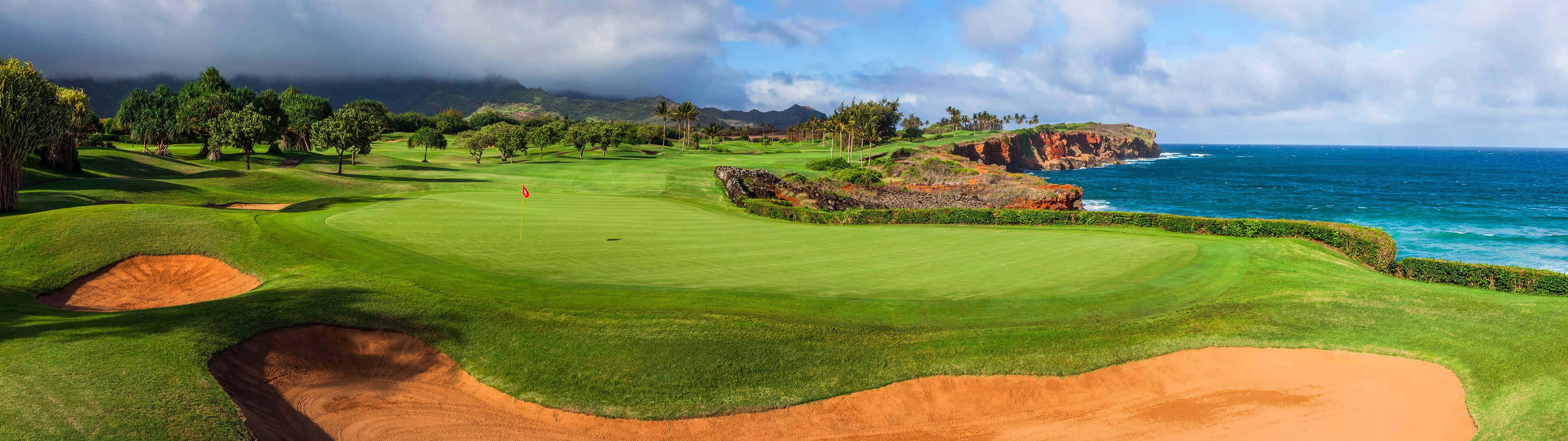 Golf 3840x1080 桌布 壁紙 — 一個鬱鬱蔥蔥的高爾夫球場擁抱著崎嶇的海岸線，在部分多雲的天空下，碧綠色的海浪拍打著紅色懸崖。