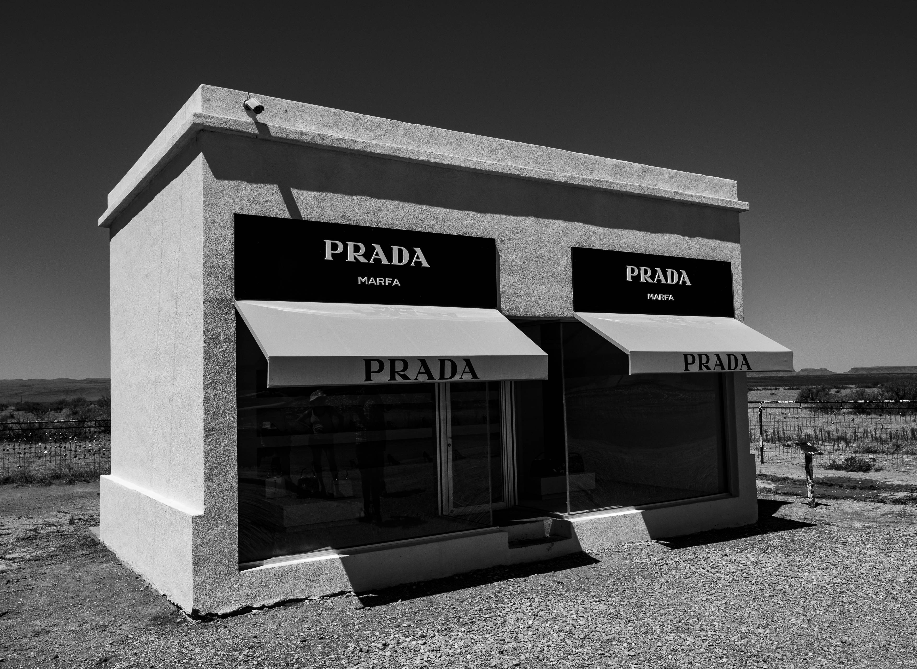 Prada 桌布 壁紙 — 一個鮮明的黑白Prada Marfa藝術裝置獨自矗立在晴朗天空下的荒涼沙漠景觀中。