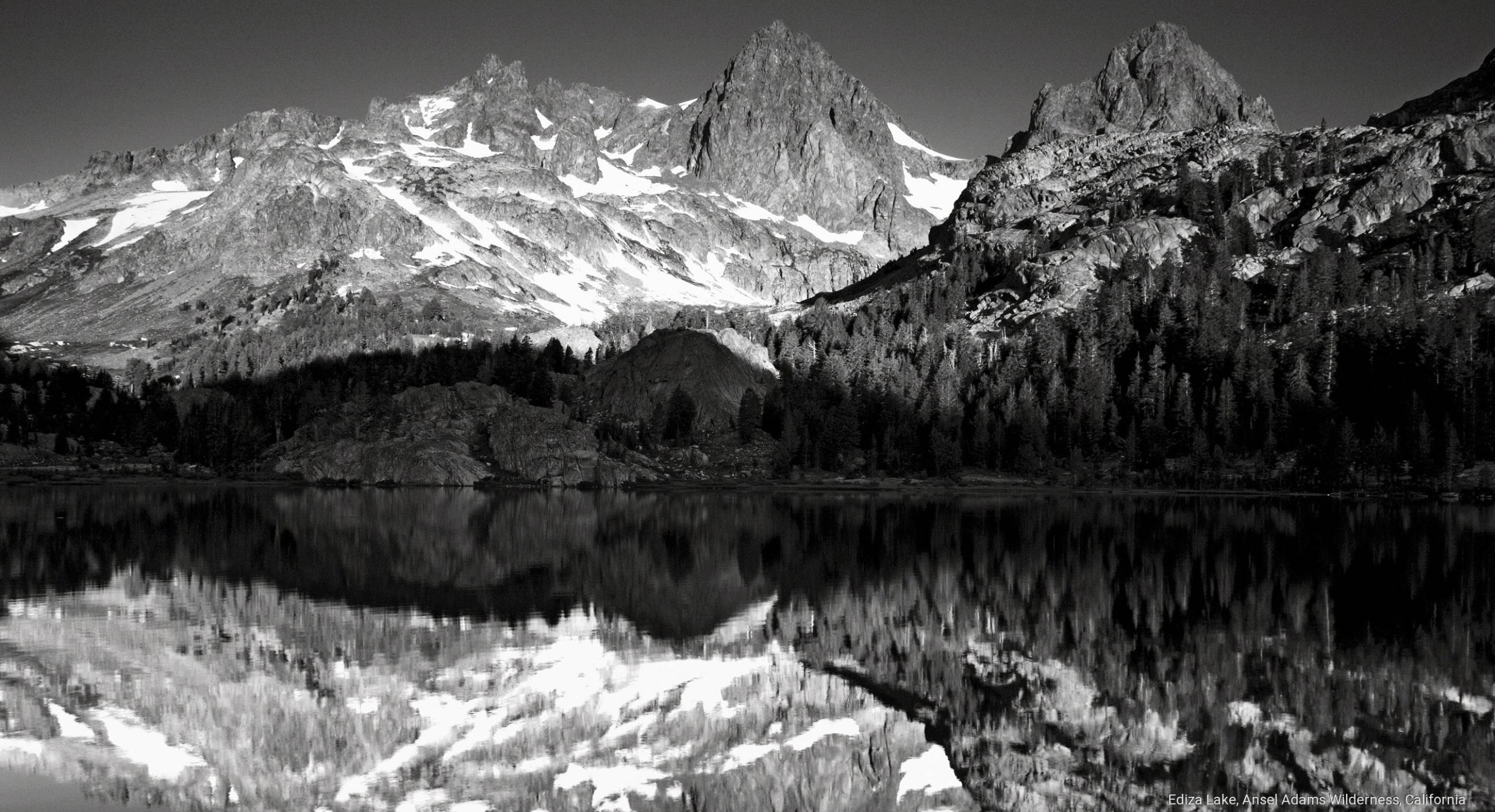 加州 桌布 壁紙 — 一個鮮明的黑白山湖場景，積雪的山峰完美地倒映在平靜的水面上，四周環繞著茂密的森林。