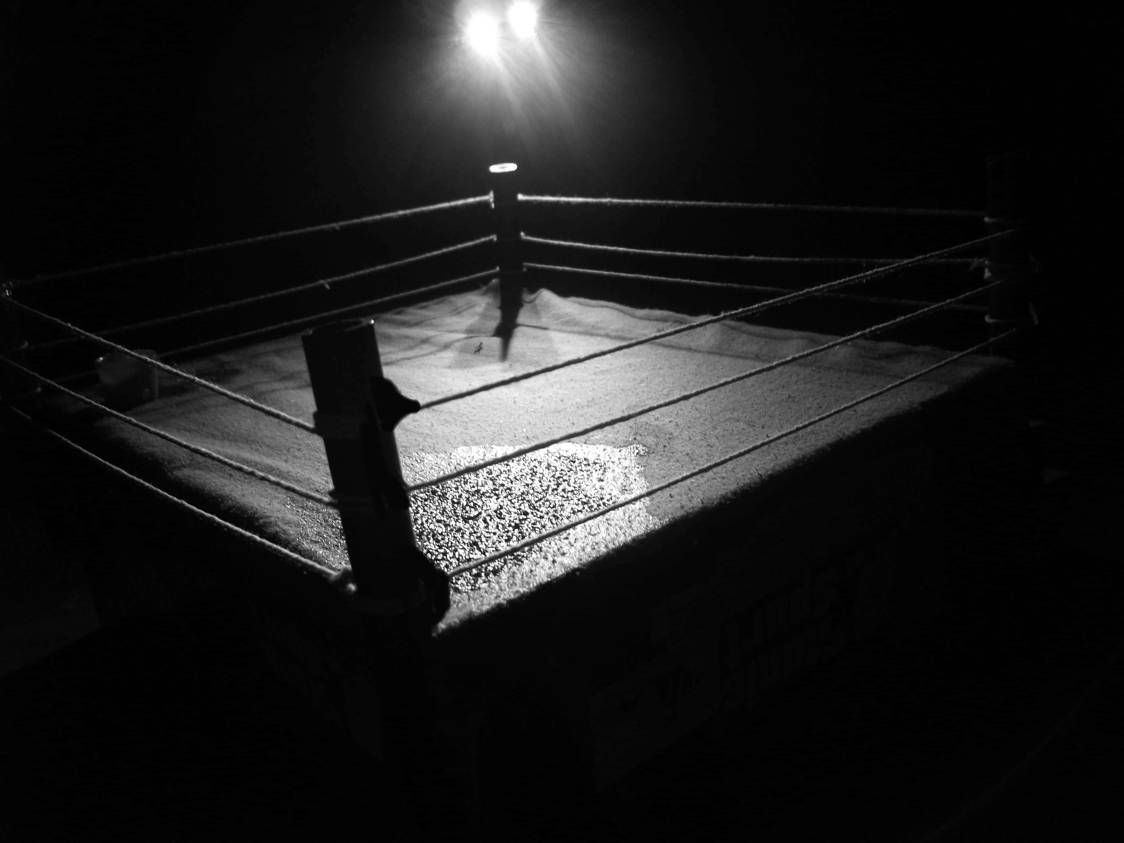 Wrestling Ring 桌布 壁紙 — 一個鮮明的黑白摔角擂台，由單一頭頂聚光燈照亮，投射出戲劇性的陰影。