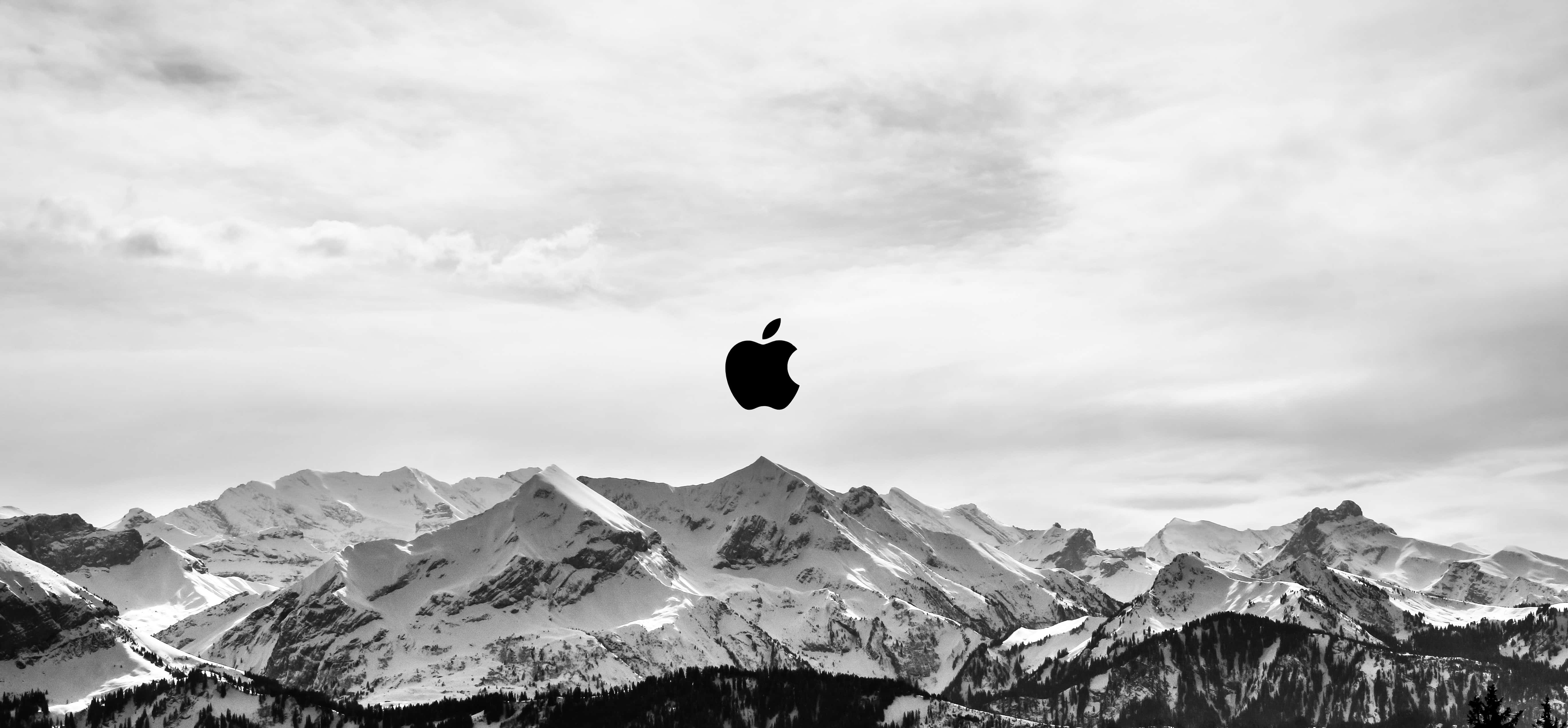 蘋果 桌布 壁紙 — 一個鮮明的黑色Apple標誌漂浮在雲層密布的天空下、白雪覆蓋的山脈之上。