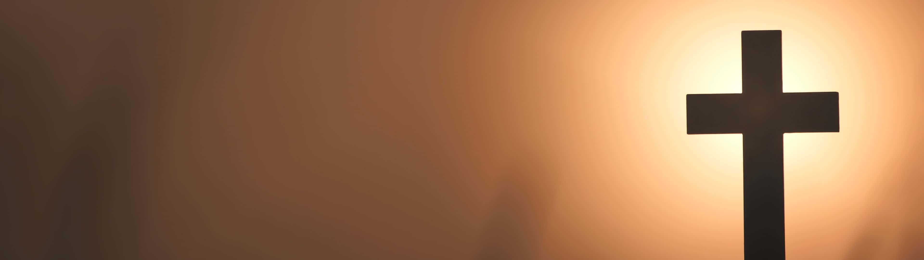3840X1080 桌布 壁紙 — 一個鮮明的黑色十字架剪影，映襯著溫暖發光的日落天空，帶有柔和的漸變色調。