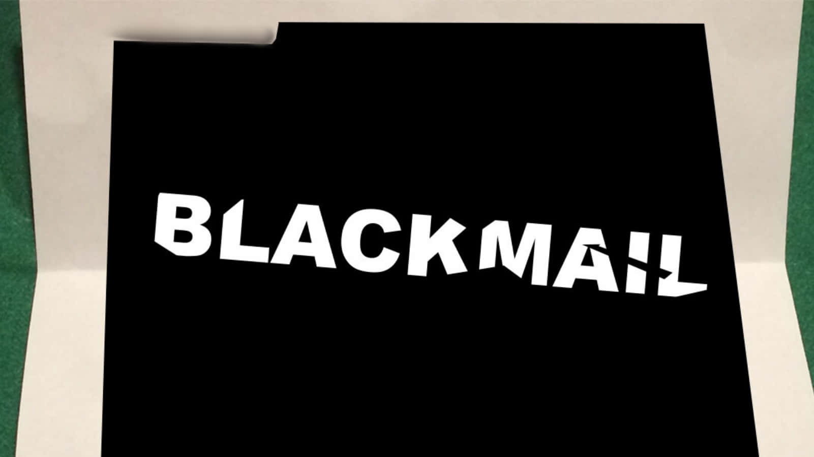Blackmail 桌布 壁紙 — 一個鮮明的黑色資料夾，上面有粗體白色「BLACKMAIL」文字，放在綠色表面上，傳達緊迫和保密。