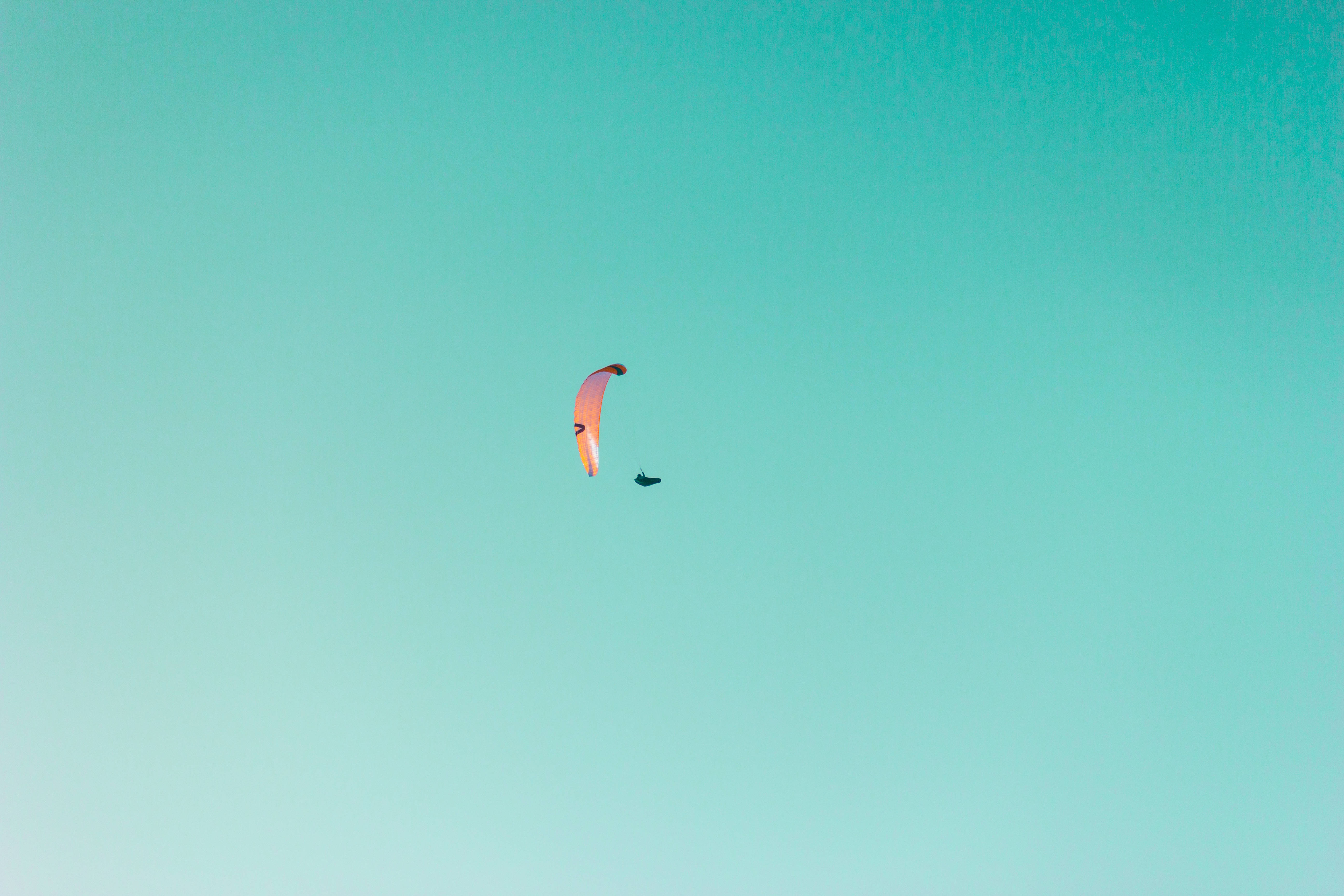 Paragliding 桌布 壁紙 — 一個鮮粉紅色的滑翔傘獨自翱翔在廣闊清澈的藍綠色天空中。