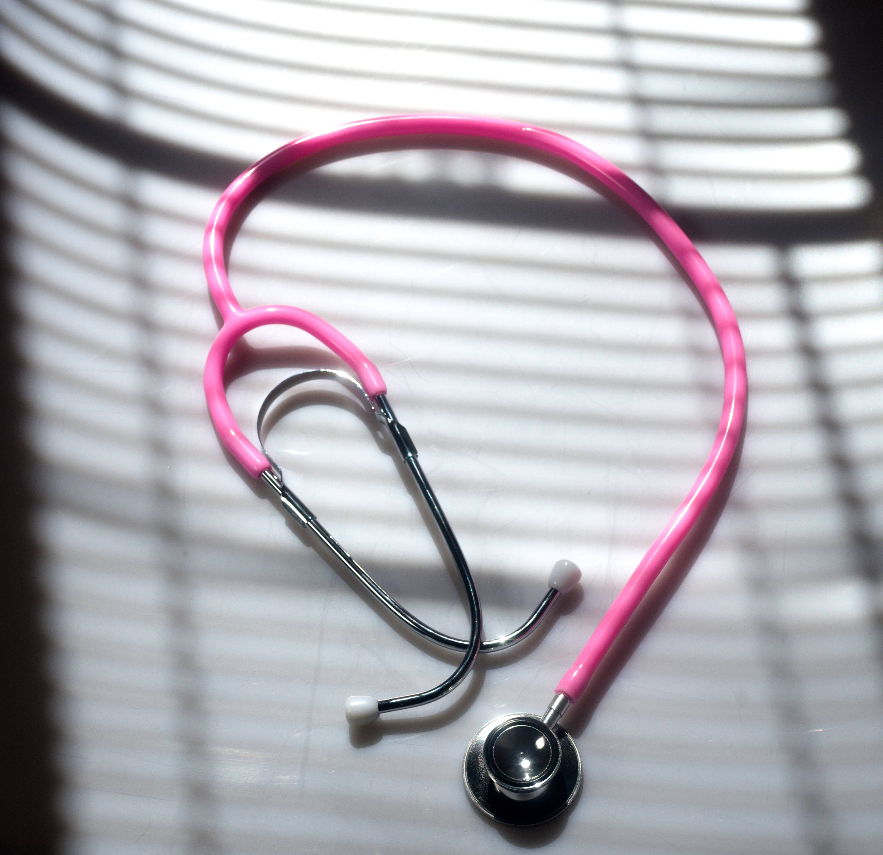 Doctors 桌布 壁紙 — 一個鮮粉紅色的聽診器放在白色表面上，條紋陽光投射出清晰的陰影。