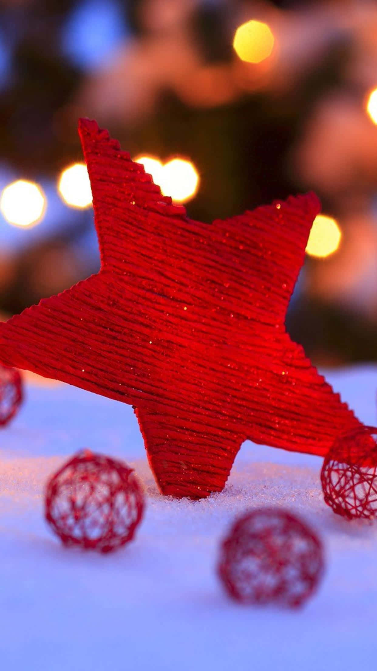Christmas Star 桌布 壁紙 — 一個鮮紅色、帶閃爍質感的星形裝飾品立在雪中，旁邊有編織的紅色球體，背景有溫暖的散景燈光閃爍。