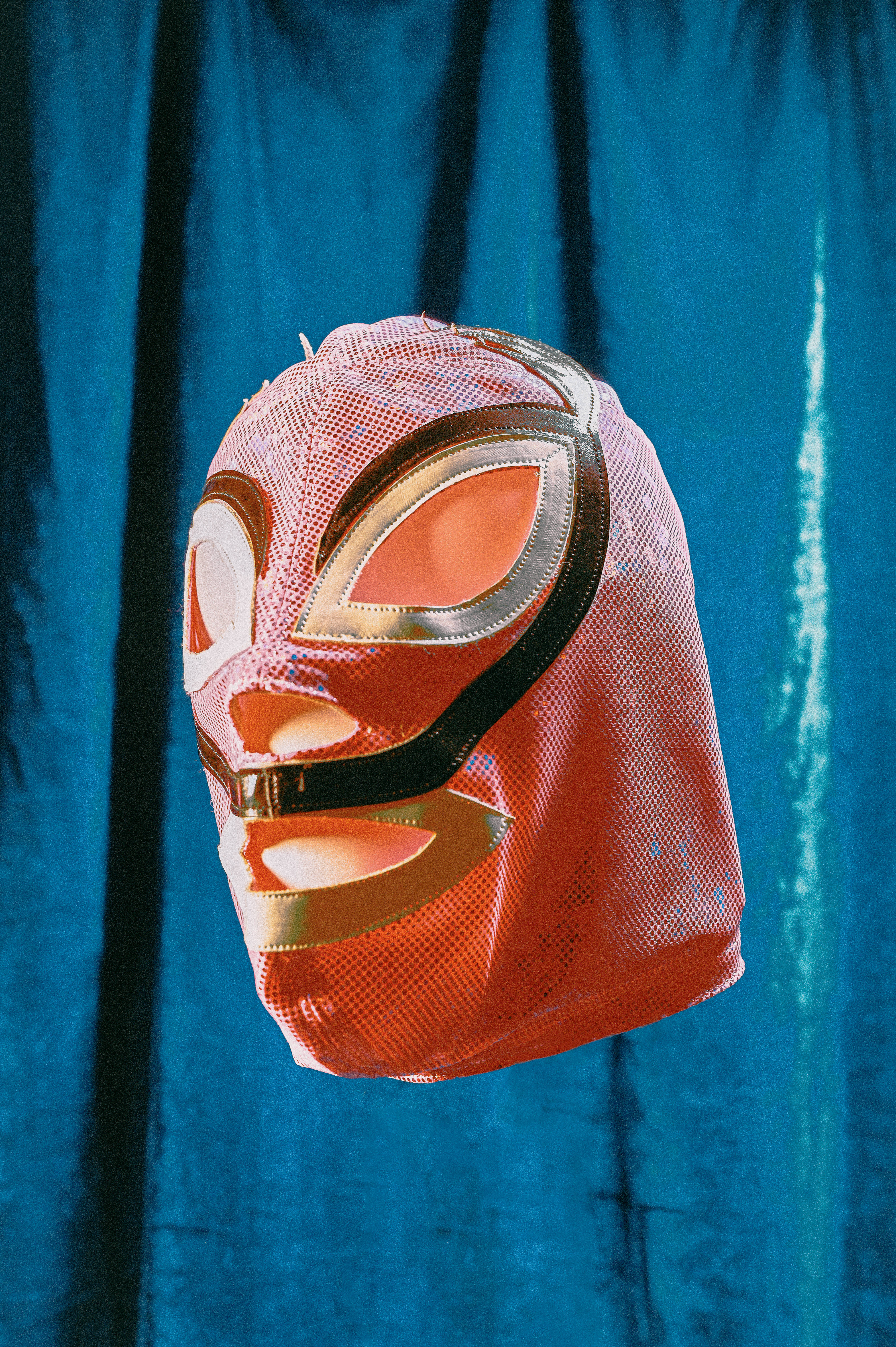 Nacho Libre 桌布 壁紙 — 一個鮮紅色帶金色飾邊的 lucha libre 面具掛在質感藍色窗簾背景前。