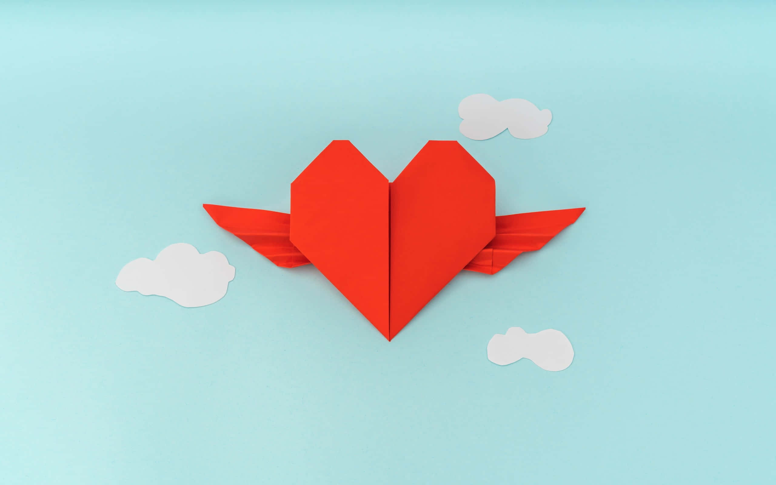Aesthetic Heart 桌布 壁紙 — 一個鮮紅色的摺紙心形長出翅膀，在柔和的藍天和 fluffy 白雲中翱翔。