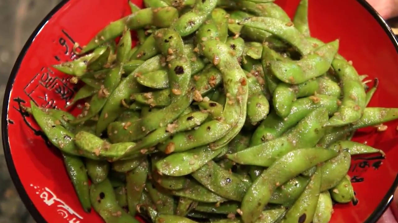 Vegetables 桌布 壁紙 — 一個鮮紅色的碗裡裝滿了閃亮的綠色毛豆莢，撒上烤芝麻和大蒜。