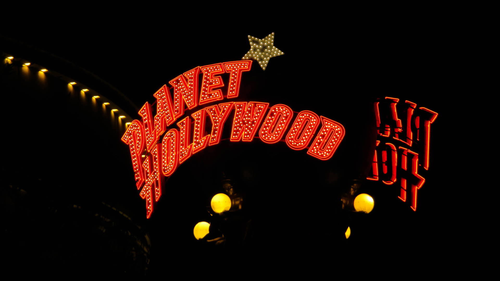 好萊塢 桌布 壁紙 — 一個鮮紅色的霓虹招牌寫著「Planet Hollywood」，在漆黑的夜空下閃耀，上方有一顆星星，下方有溫暖的燈光。