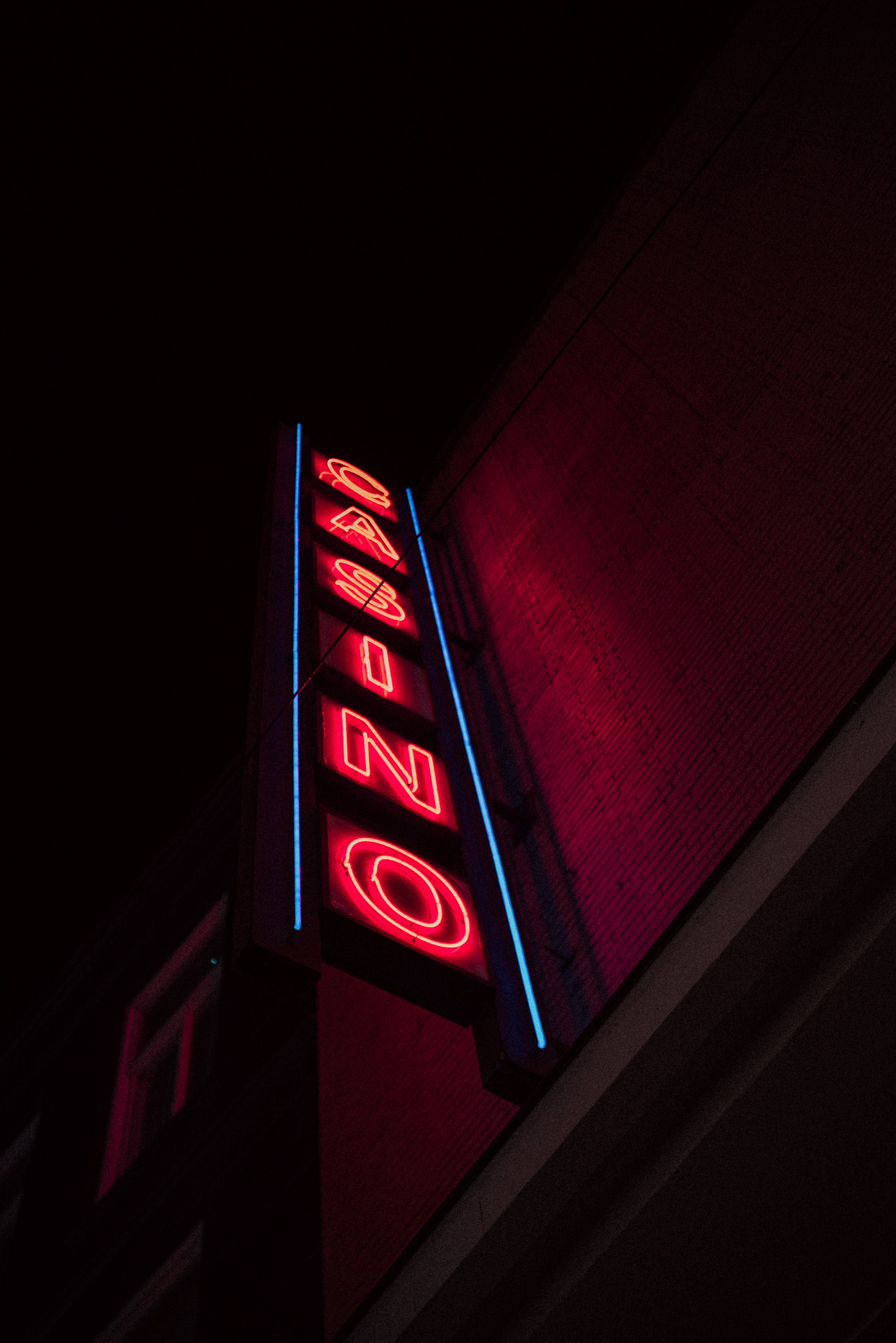 Neon Phone 桌布 壁紙 — 一個鮮紅色的霓虹賭場招牌在漆黑的夜空中發光，在建築物有紋理的牆壁上投下溫暖的光芒。