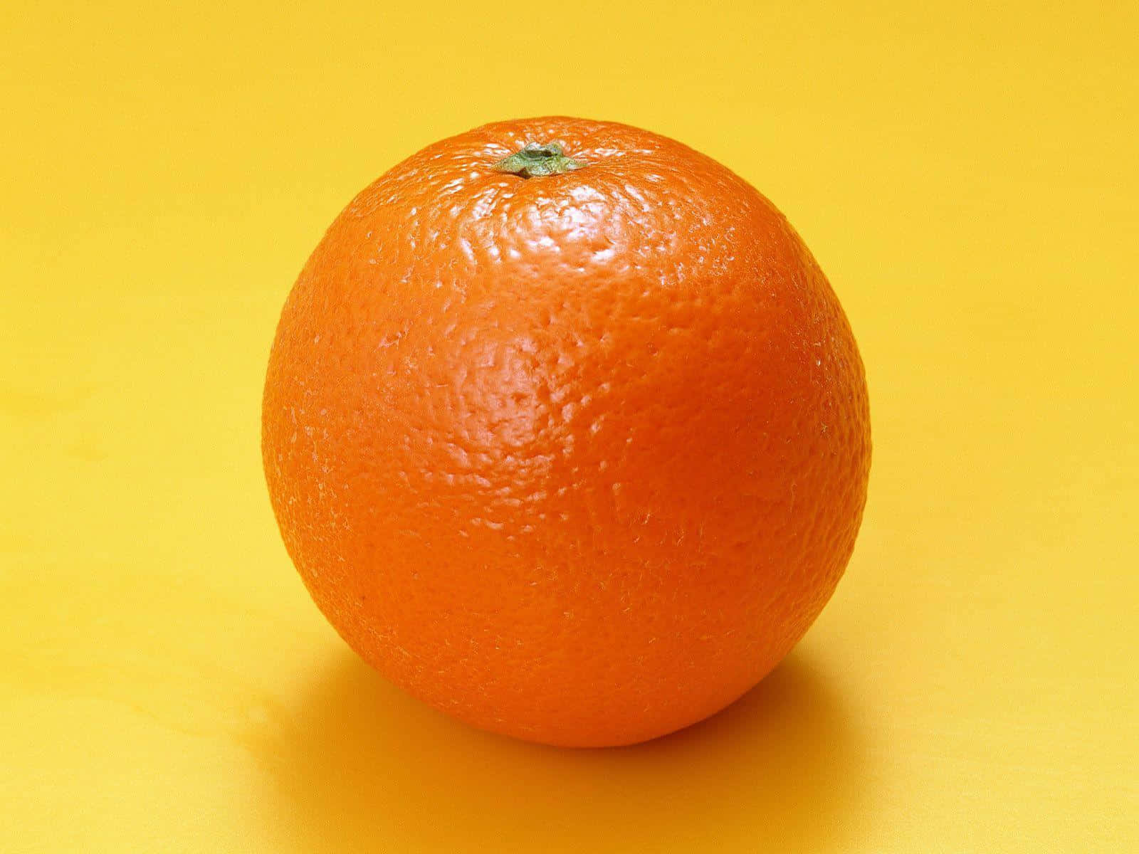 Orange Fruit 桌布 壁紙 — 一個鮮豔的柳橙，帶有紋理的果皮，居中放置在純黃色背景上。
