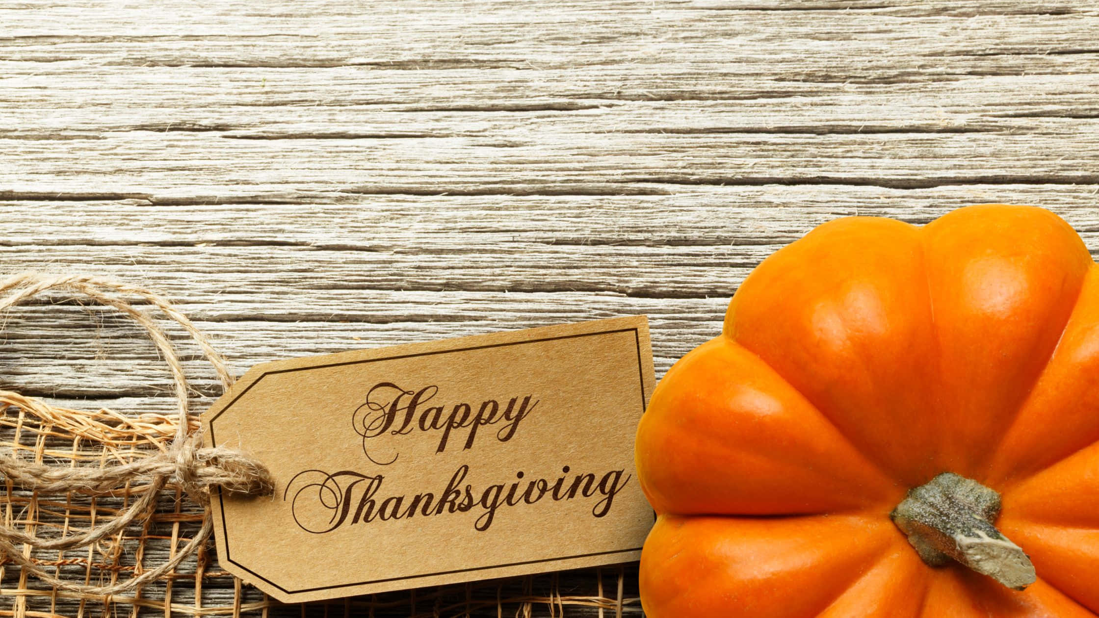 Thanksgiving Desktop 桌布 壁紙 — 一個鮮豔的橙色南瓜放在風化木上，旁邊有一個質樸的「Happy Thanksgiving」標籤。