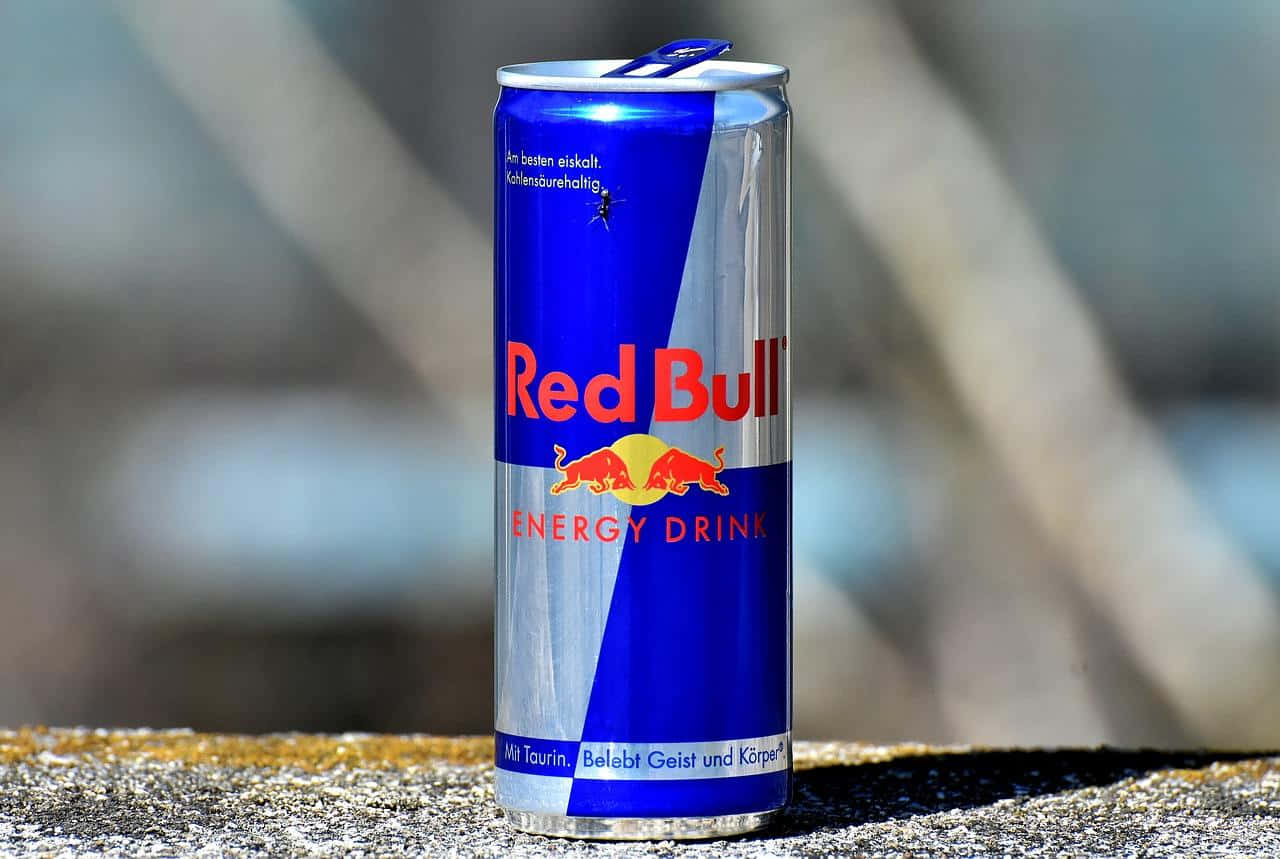 紅牛 桌布 壁紙 — 一個鮮豔的藍色和銀色Red Bull能量飲料罐直立於有紋理的石頭表面上，背景是模糊的自然景色。