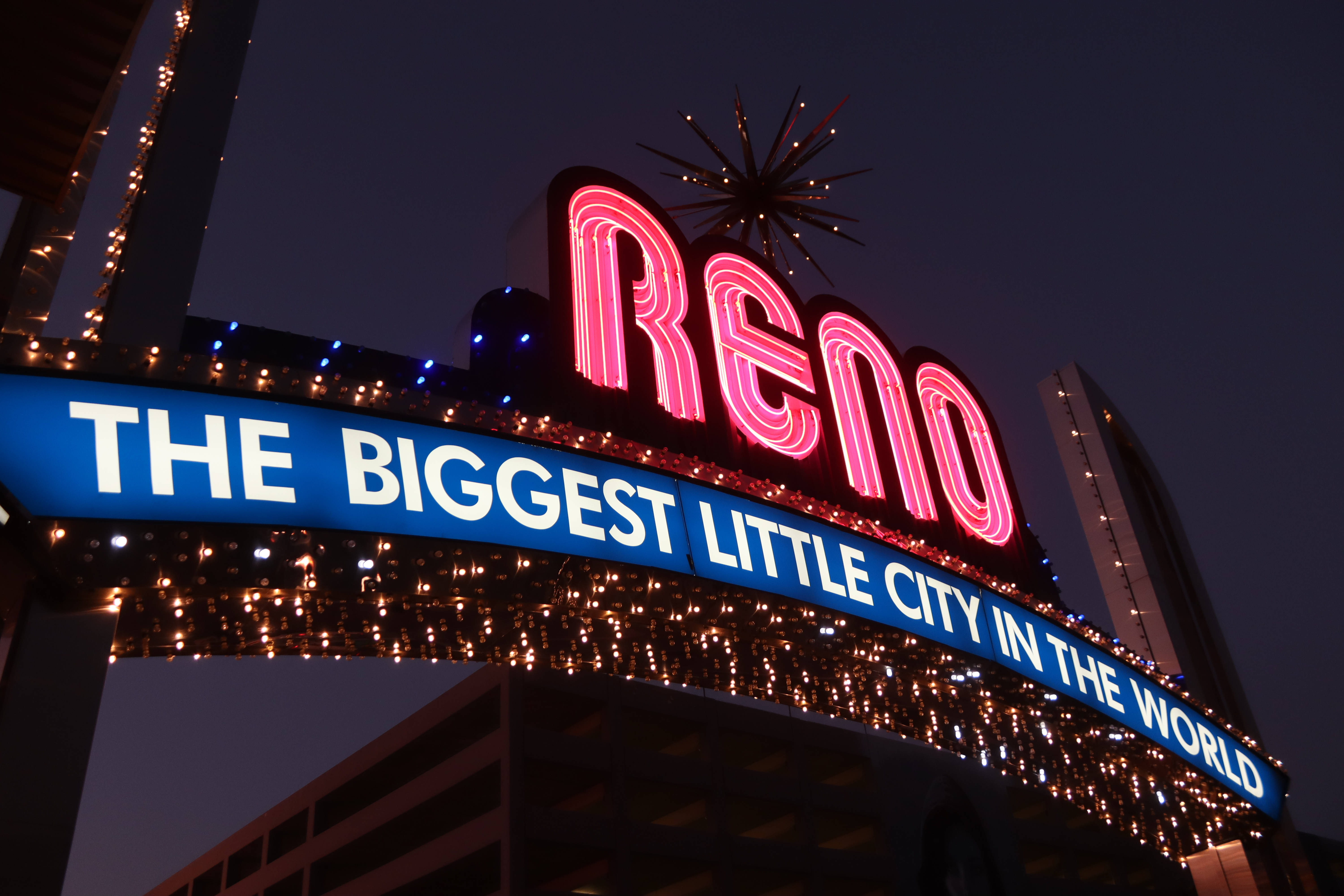 Night Aesthetic 桌布 壁紙 — 一個鮮豔的霓虹燈牌，上面寫著「Reno」和「The Biggest Little City in the World」，在漆黑的夜空中閃耀。