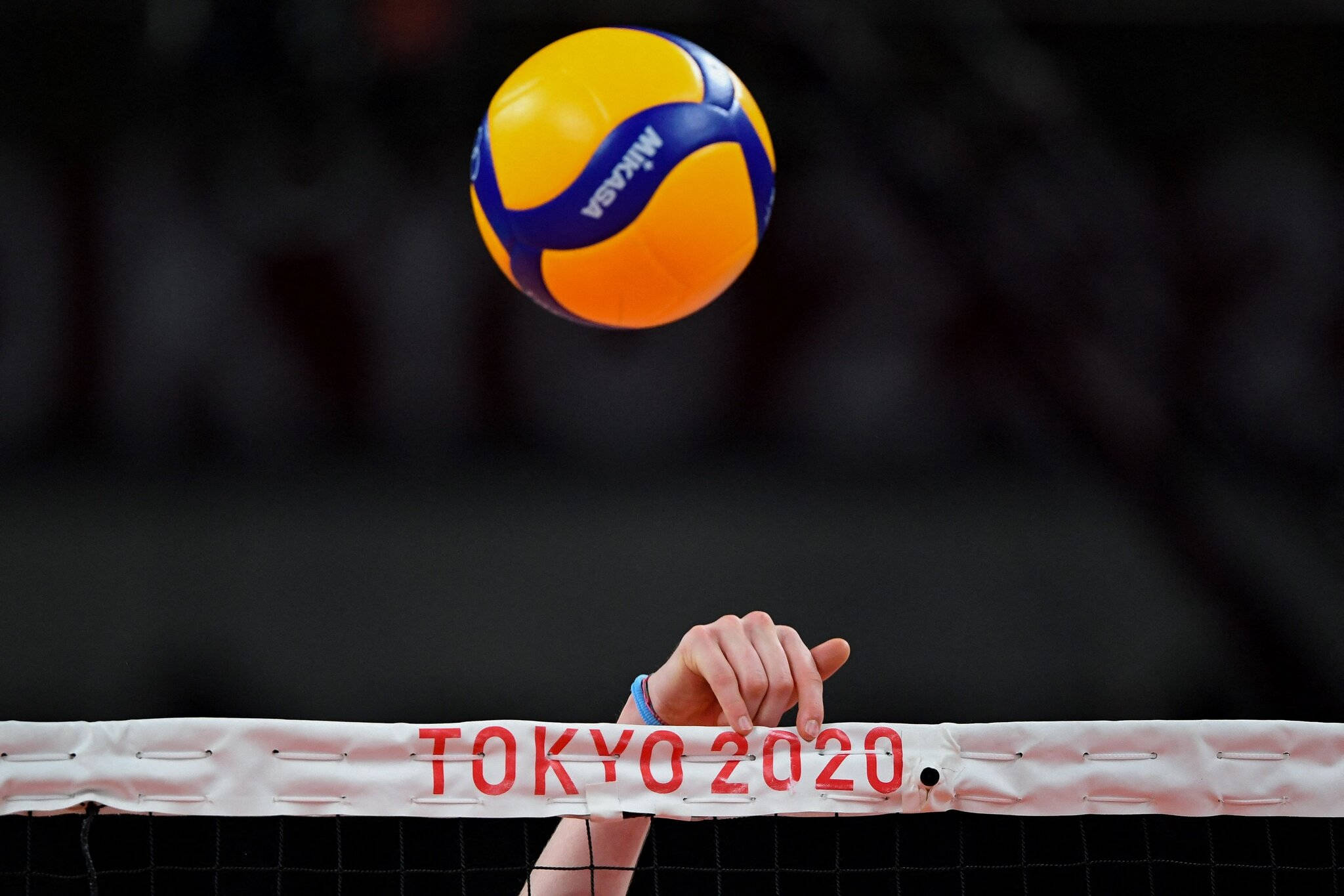 筆電 桌布 壁紙 — 一個鮮黃色和藍色的 Mikasa 排球懸浮在網上，帶有 'TOKYO 2020' 文字，一隻手抓住網的頂部邊緣。