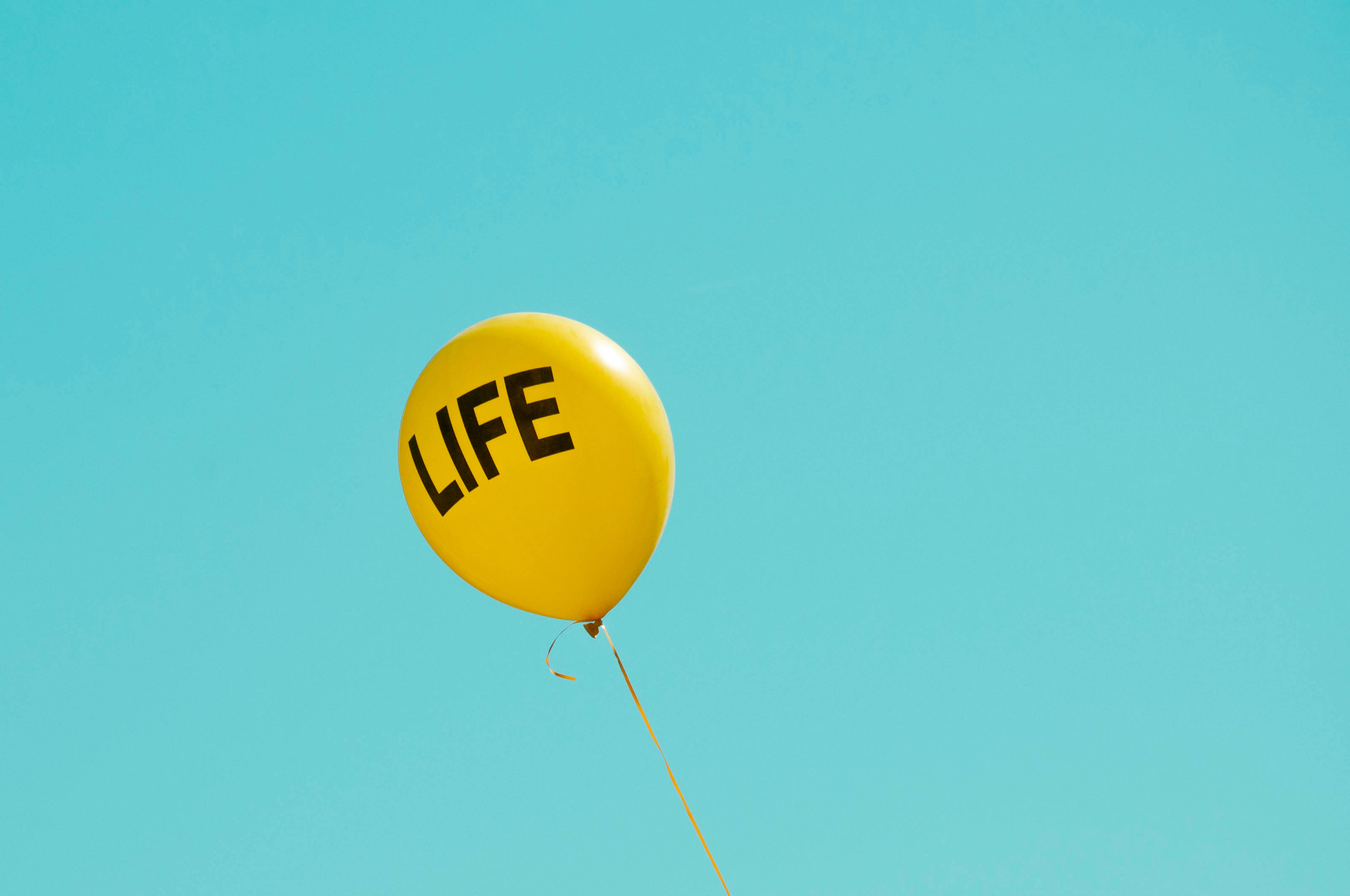 Balloon 桌布 壁紙 — 一個鮮黃色氣球，上面有「LIFE」字樣，漂浮在清澈的藍綠色天空上。
