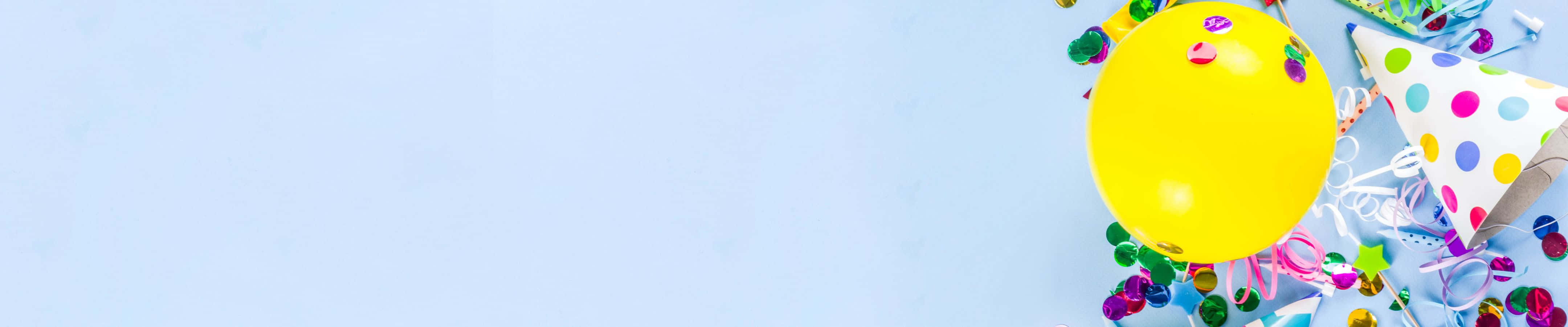 4320x900 桌布 壁紙 — 一個鮮黃色氣球和彩色派對帽放在淺藍色表面上，周圍環繞著節日五彩紙屑。
