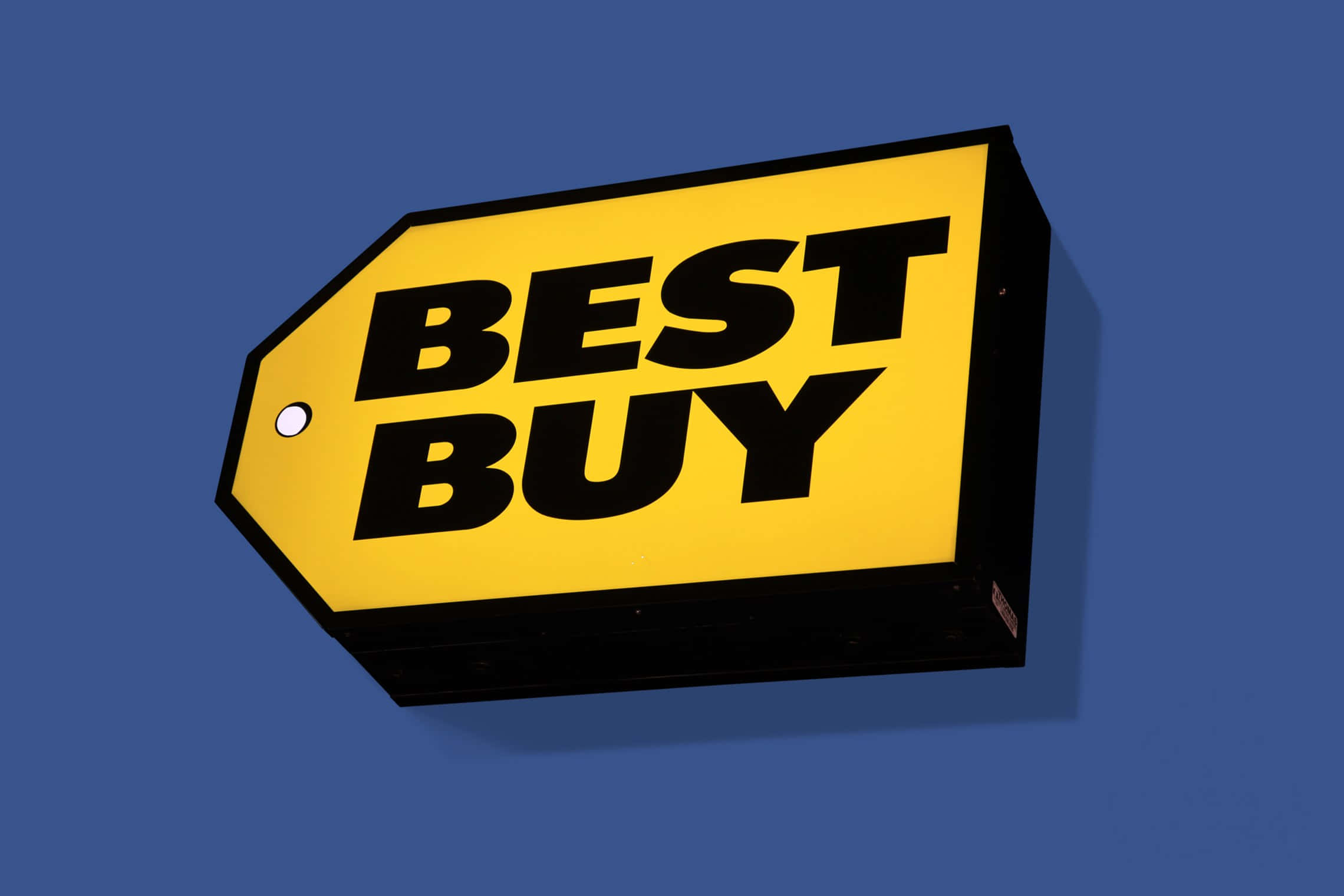 Best Buy 桌布 壁紙 — 一個鮮黃色的Best Buy價格標籤牌，帶有粗體黑色文字，掛在純藍色牆壁上。