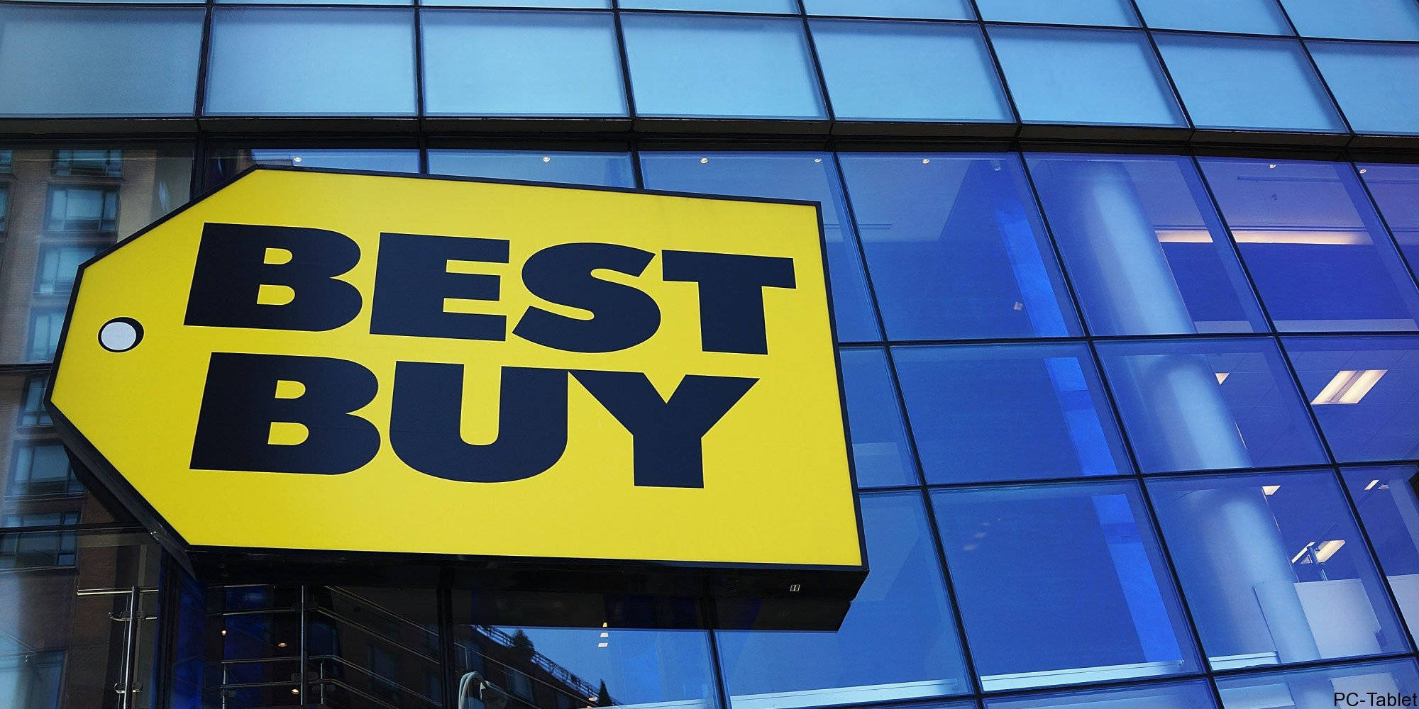 buy 桌布 壁紙 — 一個鮮黃色的Best Buy標誌醒目地掛在現代玻璃建築外牆上，反射著城市燈光。