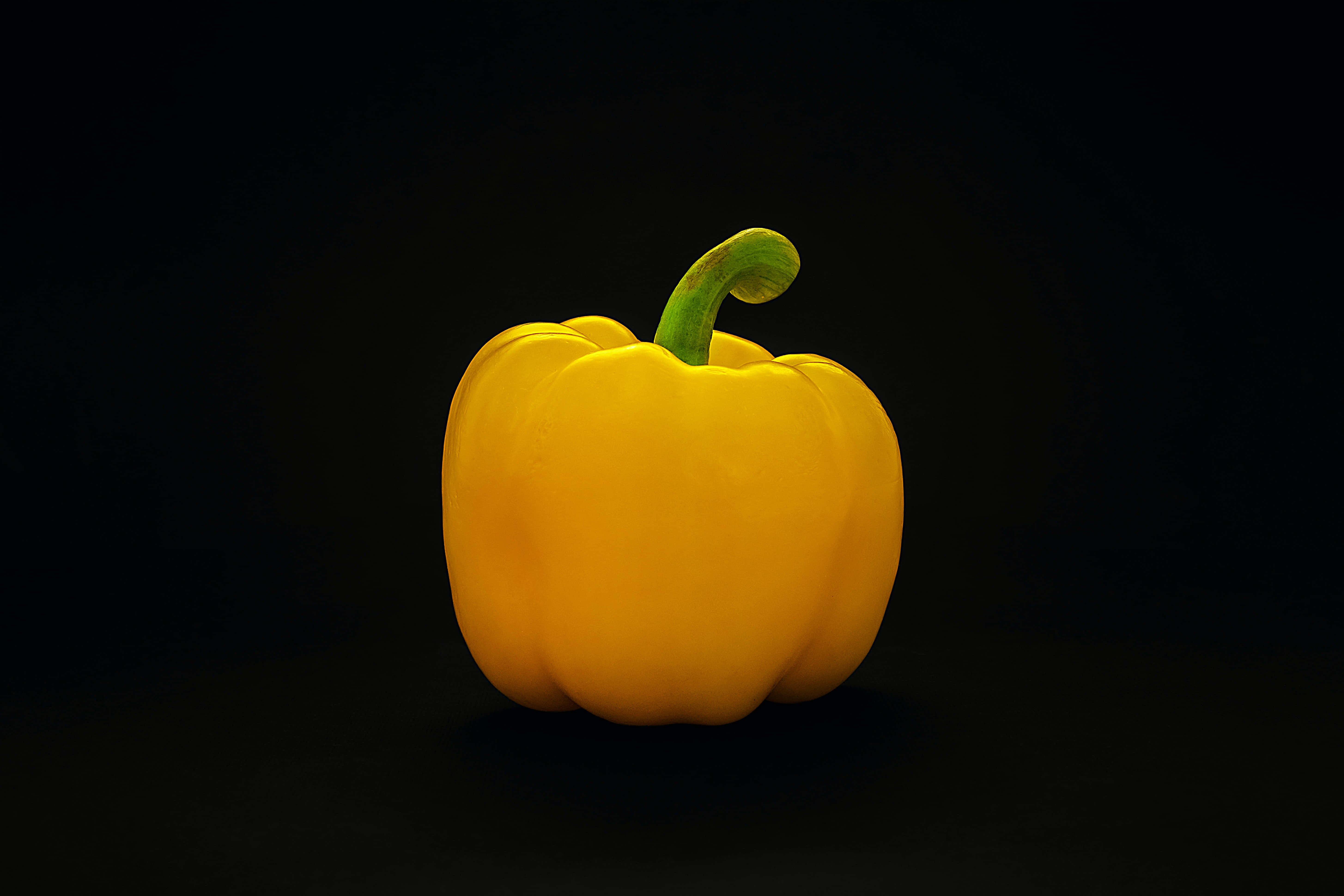 Yellow Bell Pepper 桌布 壁紙 — 一個鮮黃色的甜椒，帶有綠色莖部，孤立在深黑色背景前。