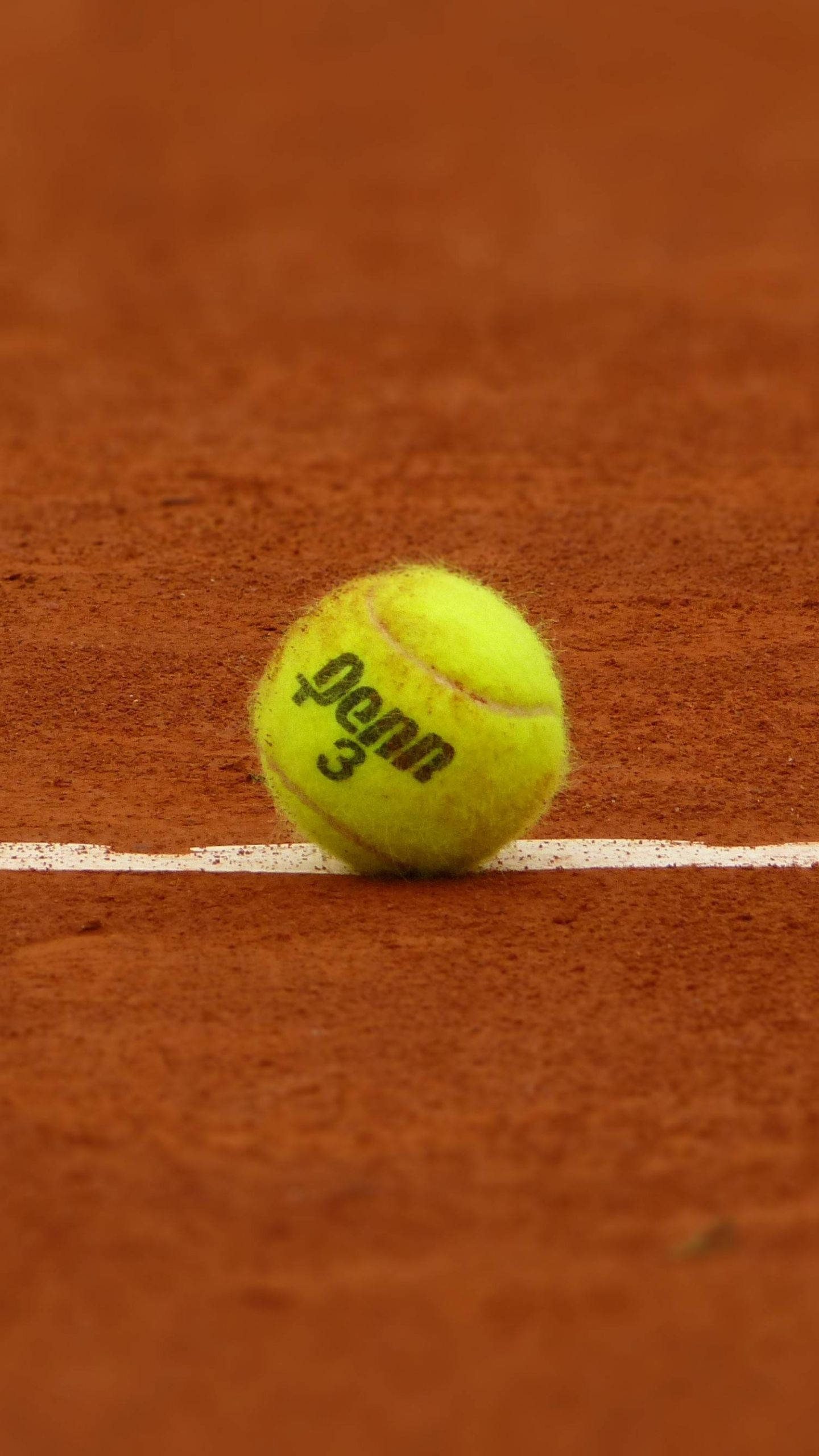 Tennis Ball 桌布 壁紙 — 一個鮮黃色的網球放在紅土球場上，靠近一條清晰的白色界線。