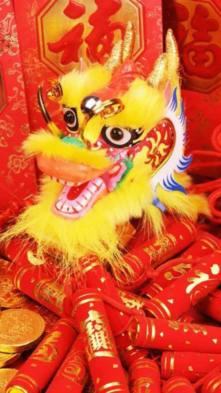 New Year 桌布 壁紙 — 一個鮮黃色的舞獅頭，周圍環繞著紅色鞭炮和金幣，背景是喜慶的紅色。