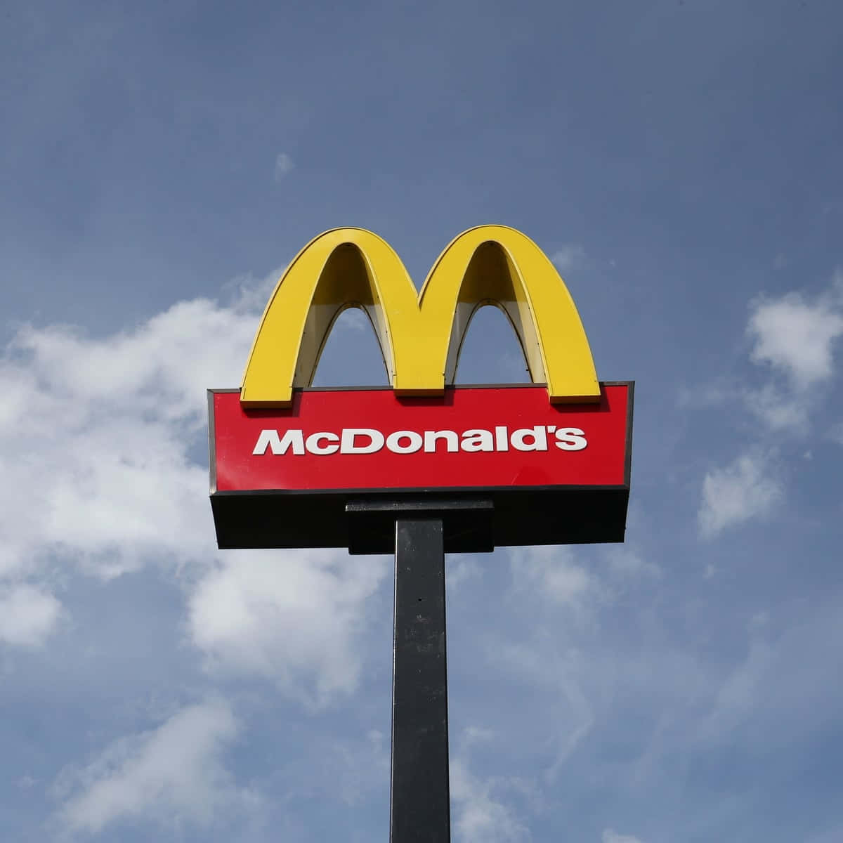 Mcdonalds 桌布 壁紙 — 一個鮮黃色的麥當勞拱門標誌位於紅色招牌上，襯托著部分多雲的藍天。
