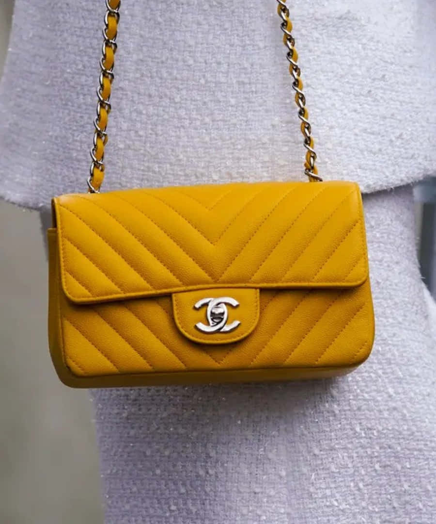 Chanel 桌布 壁紙 — 一個鮮黃色菱格紋Chanel手袋搭配銀色鏈條肩帶，放置在帶有紋理的灰色衣物上。