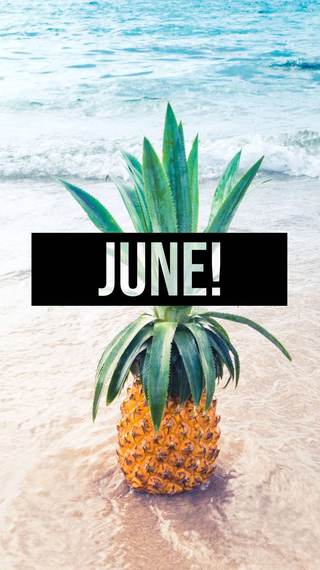 June 桌布 壁紙 — 一個鳳梨位於沙灘的淺海水域，有輕柔的海浪和粗體的「JUNE!」文字疊加。