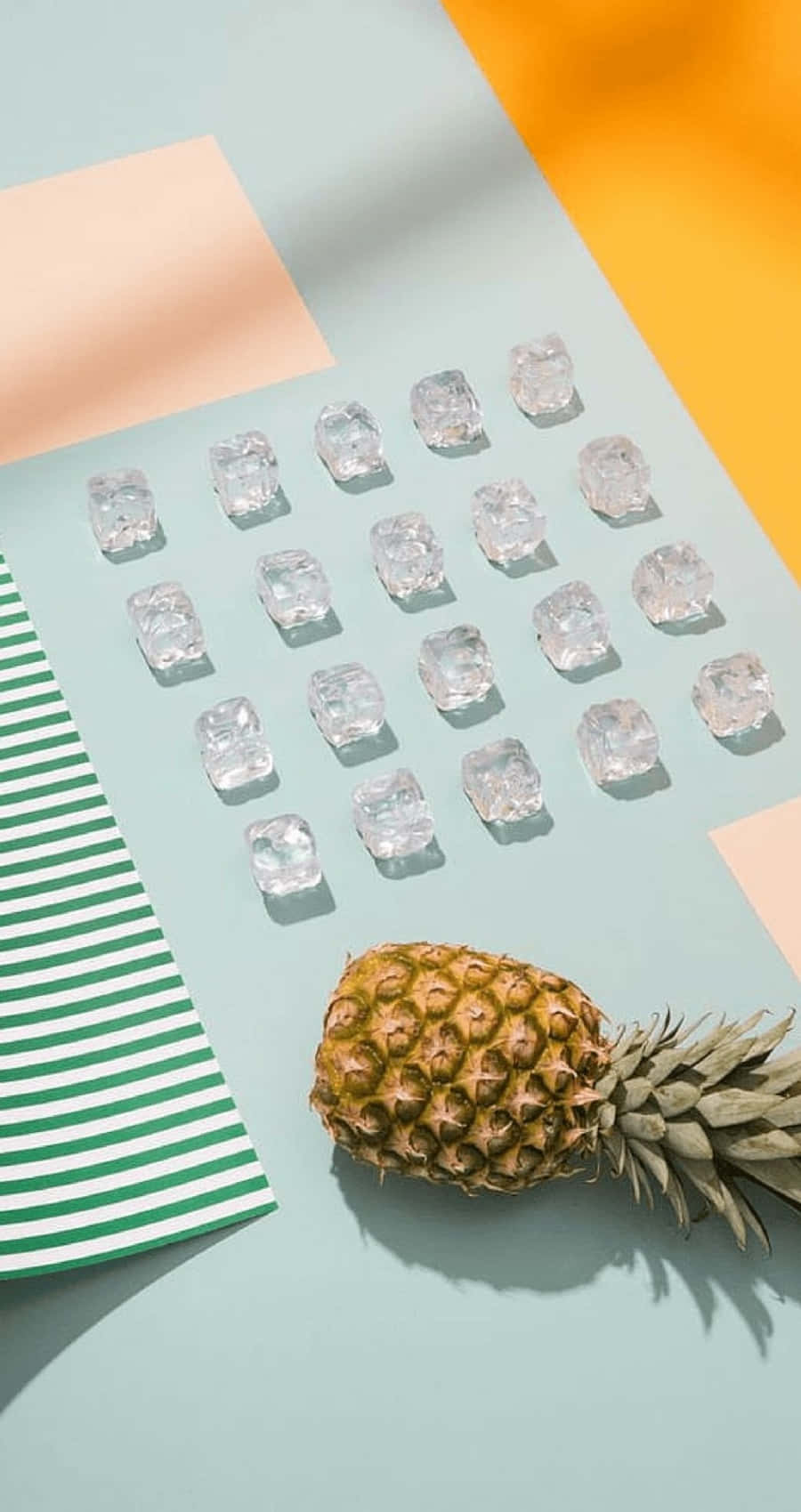 美學 iPhone 壁紙 桌布 壁紙 — 一個鳳梨放在冰塊網格旁邊，背景是粉彩色，帶有幾何色塊和條紋紙。